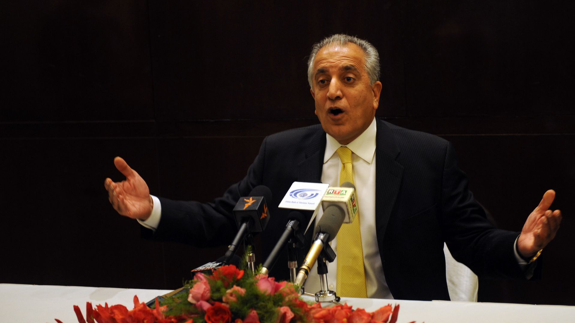 Zalmay Khalilzad speaks and gestures from a table with mics