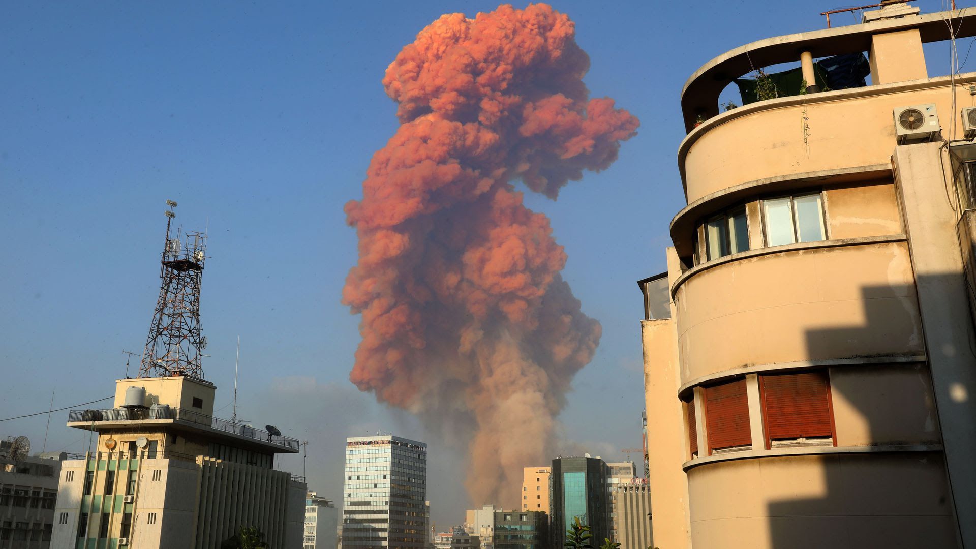 An orange-reddish smoke cloud seen in between buildings after an explosion in Beirut