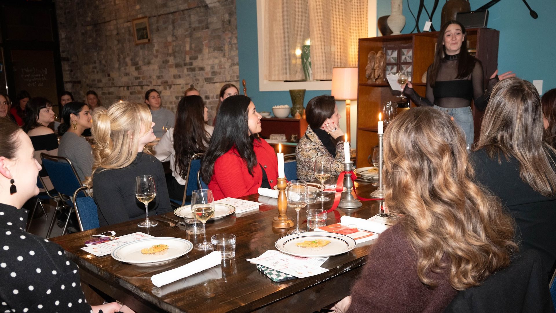Table with people sitting around it and looking up at a woman talking