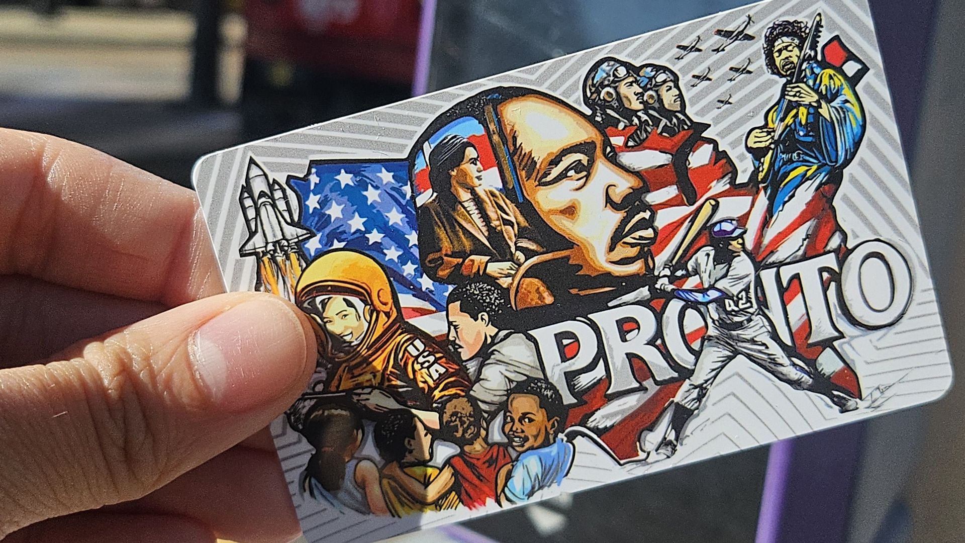 Hand holding card with colorful illustrations including astronauts, children, historical figures, a batter, and American flag background with word "PRONTO" in bold letters.