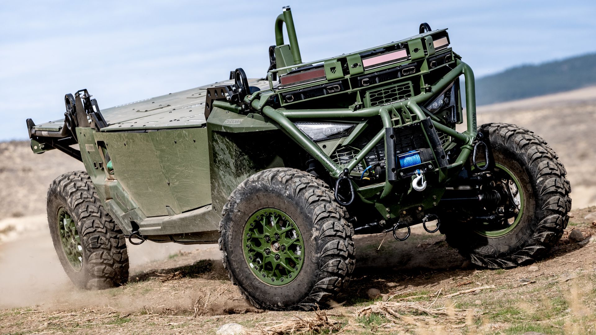 Military green off-road vehicle with rugged features and large tires on a dirt trail.