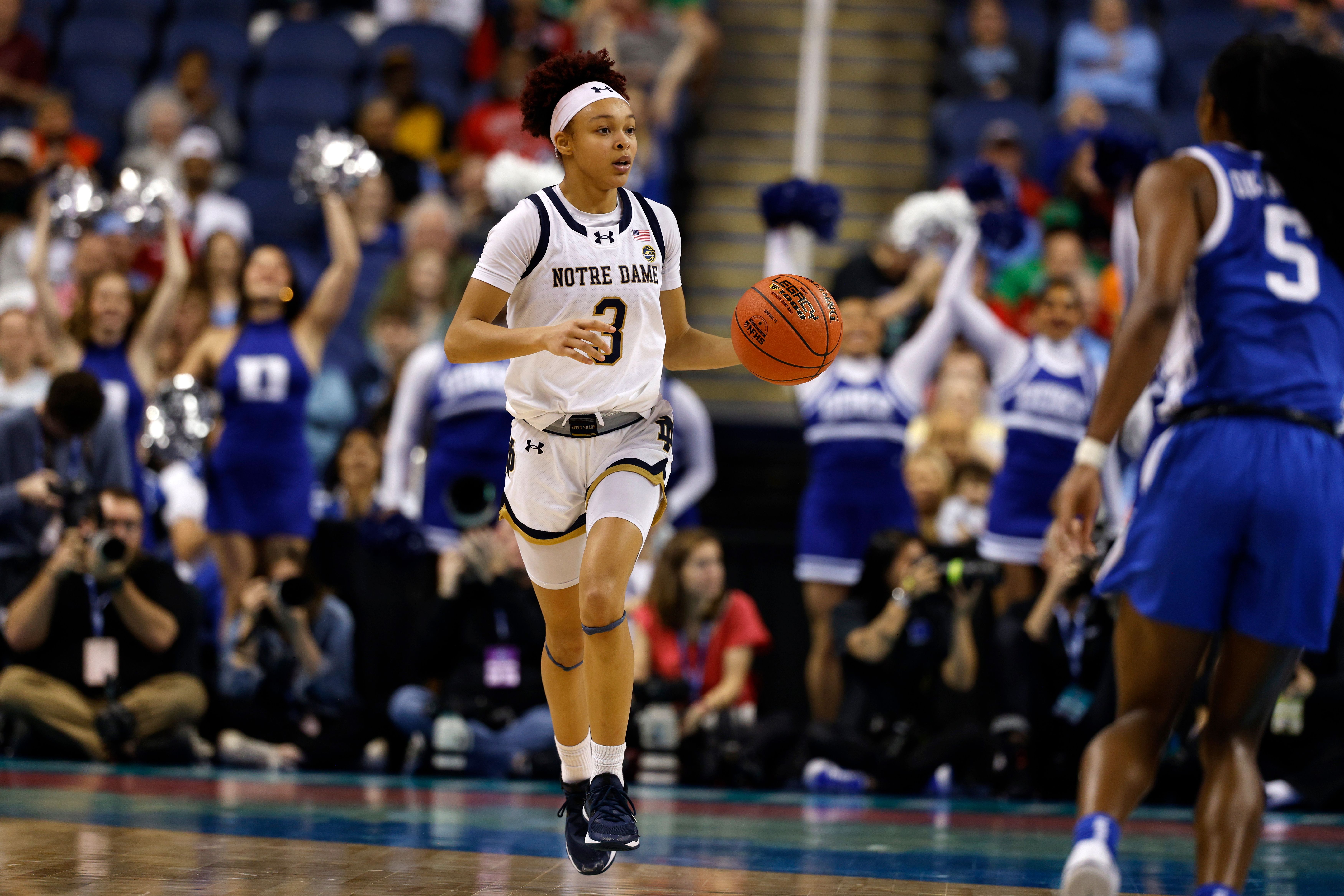 Photo of a woman dribbling a basketball on a court.