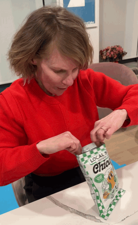 GIF of Carrie Shepherd in a red sweater opening a bag of chips and eating a green chip.