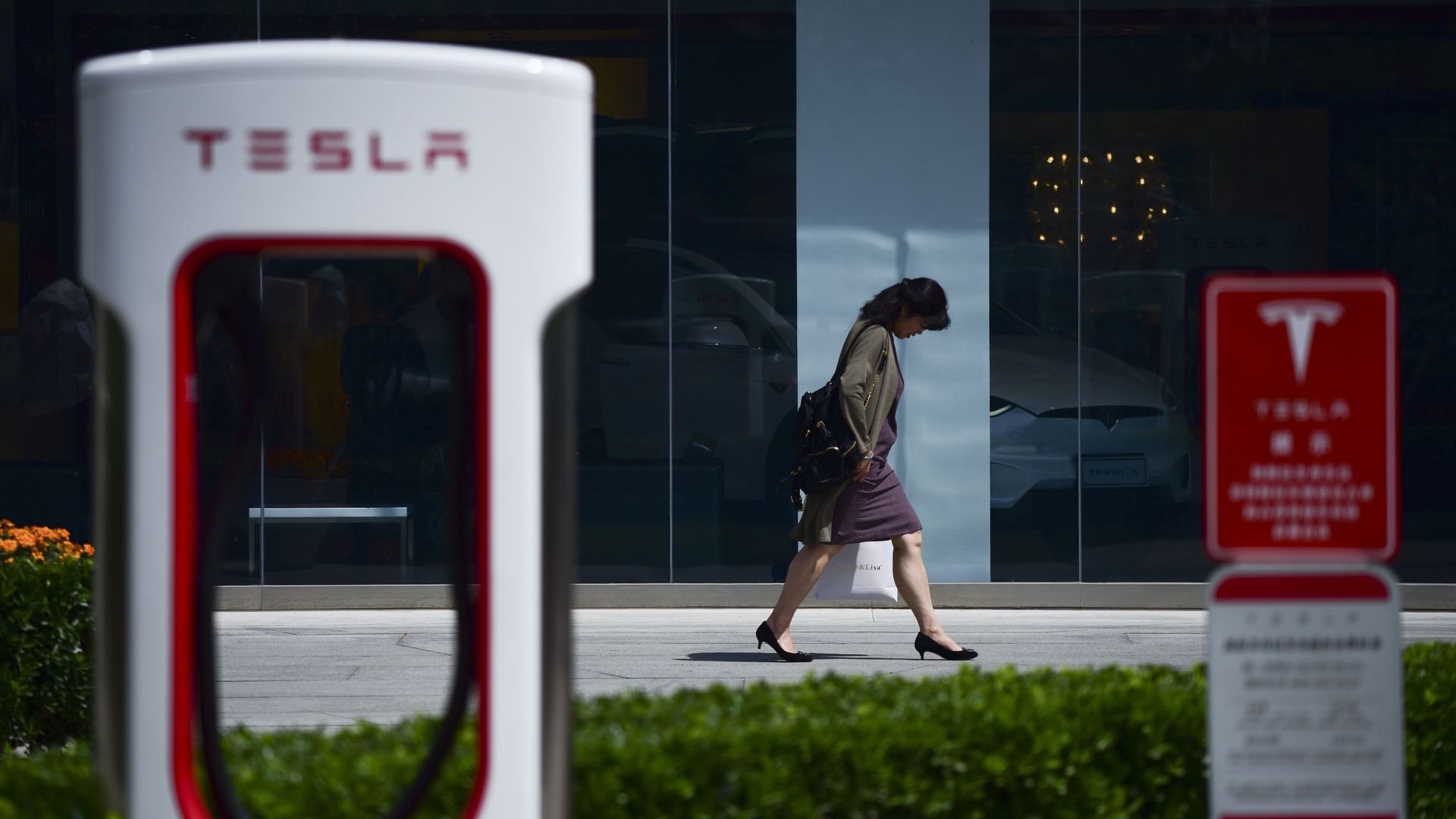 In this image, a woman walks past a Tesla charging port.