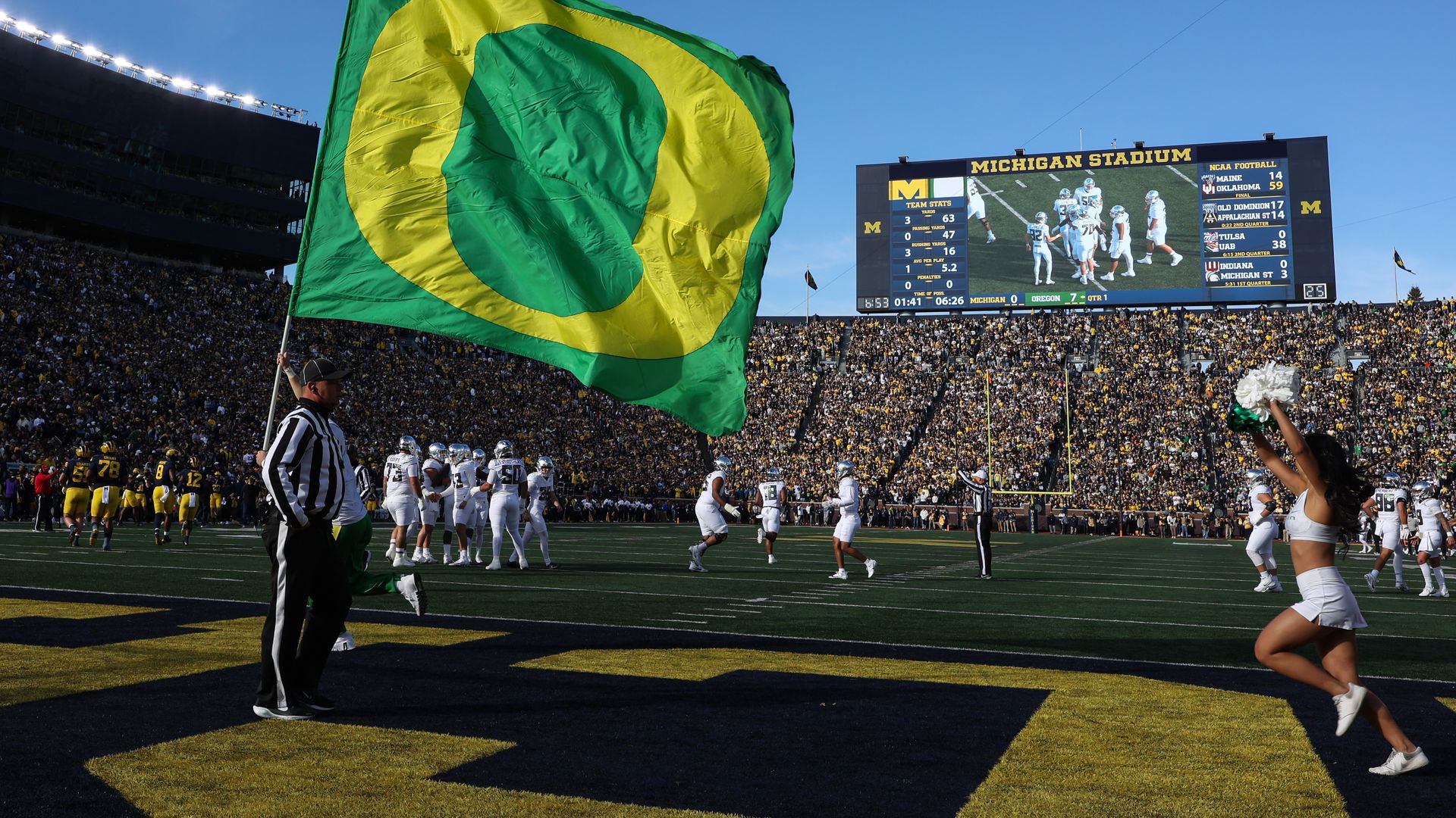A large University of Oregon flag is seen flying on the field in a packed football stadium.