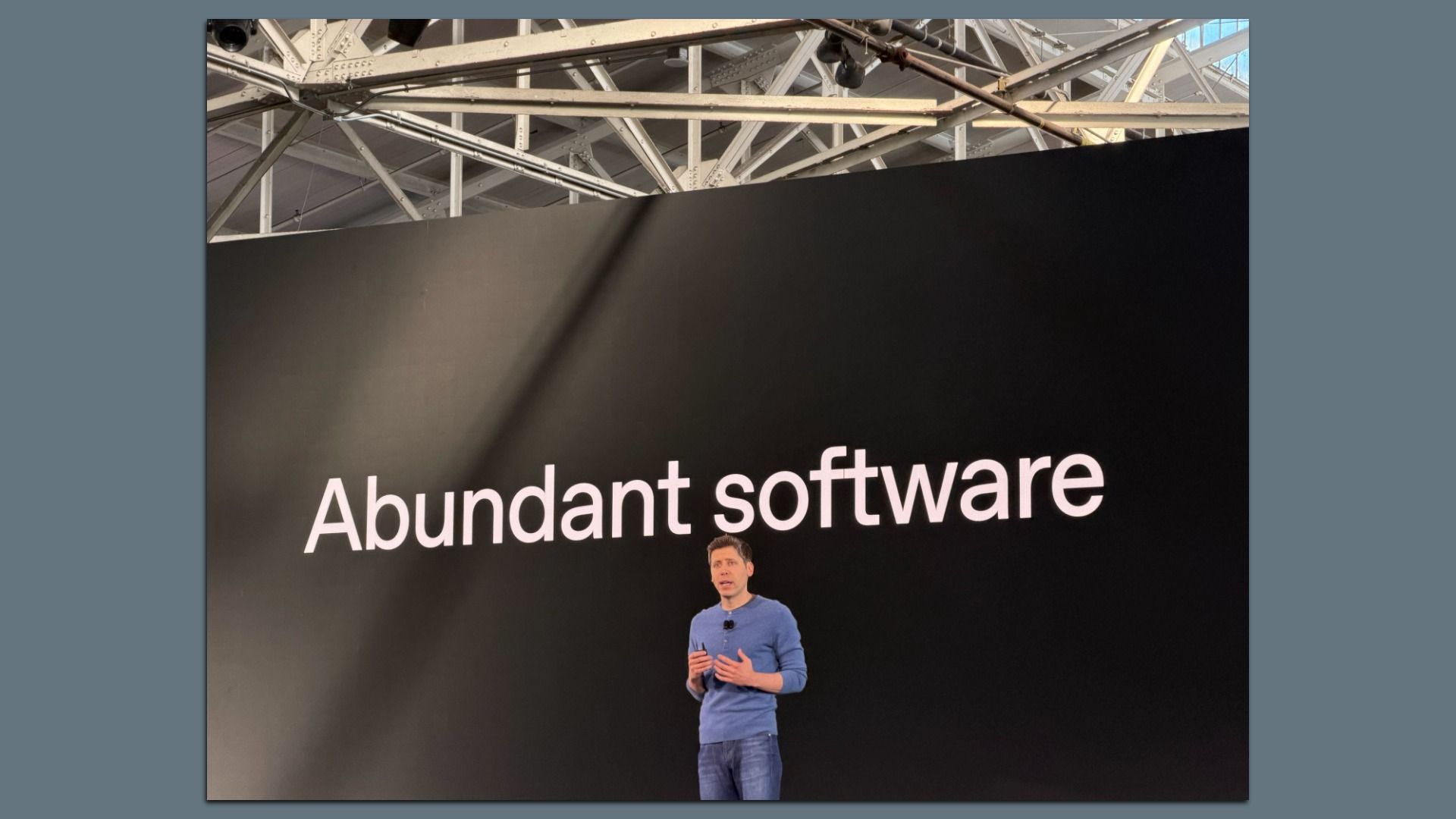 A man in a blue sweater and jeans stands on stage speaking in front of a large black screen displaying the words "Abundant software" in white text.
