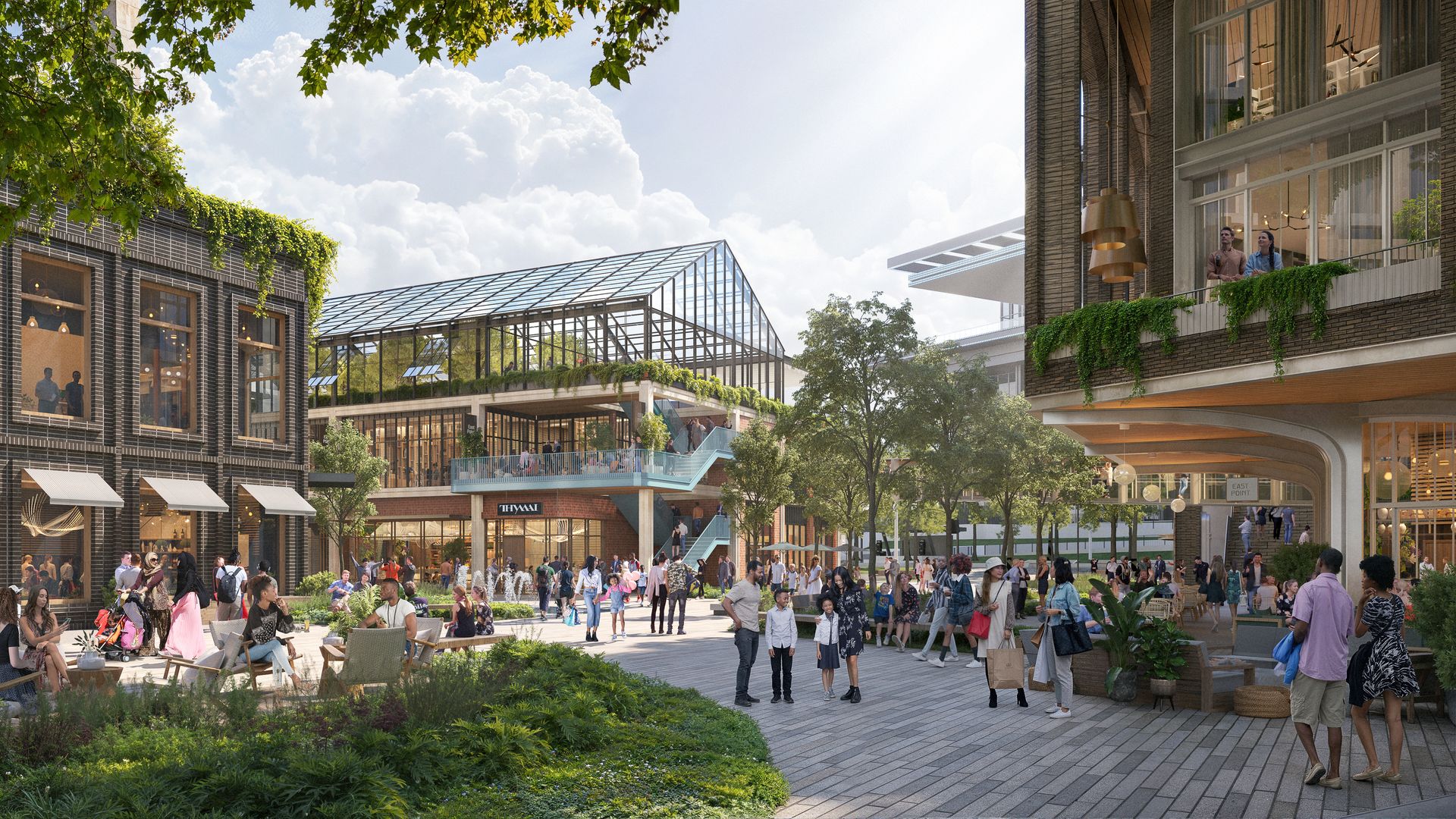 Busy urban plaza filled with people; brick buildings, greenery, and a glass greenhouse at center. A clear sky, trees overhead, and a second-story walkway frame the scene.