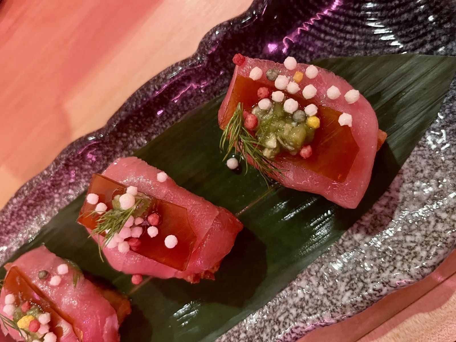 Pieces of pinkish sushi on a green leaf.