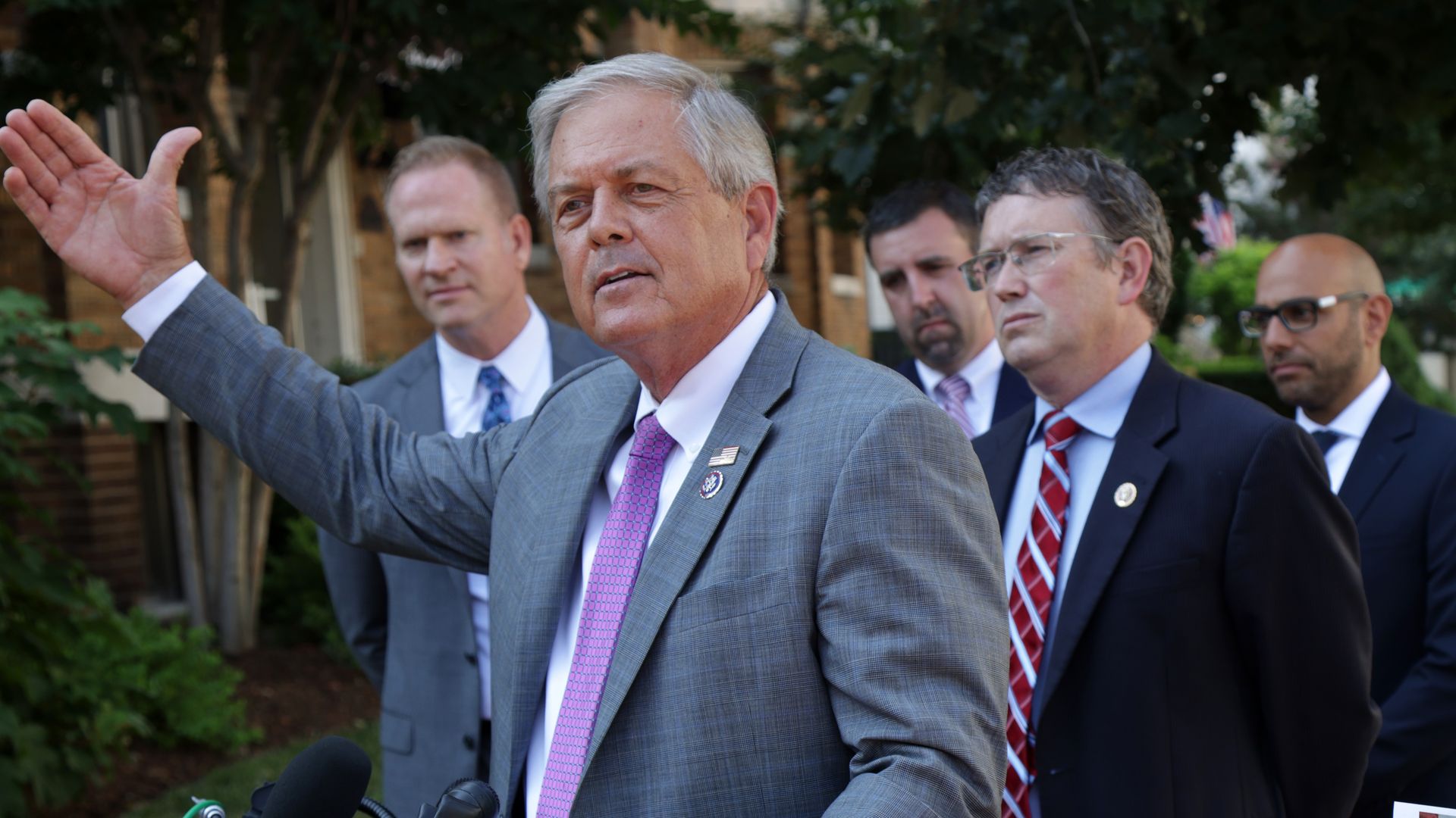 Reps. Ralph Norman (R-S.C.), wearing a gray suit; white shirt; and purple tie, and Thomas Massie (R-Ky.), wearing a blue suit; blue shirt and red tie, speak at an outdoor press conference.