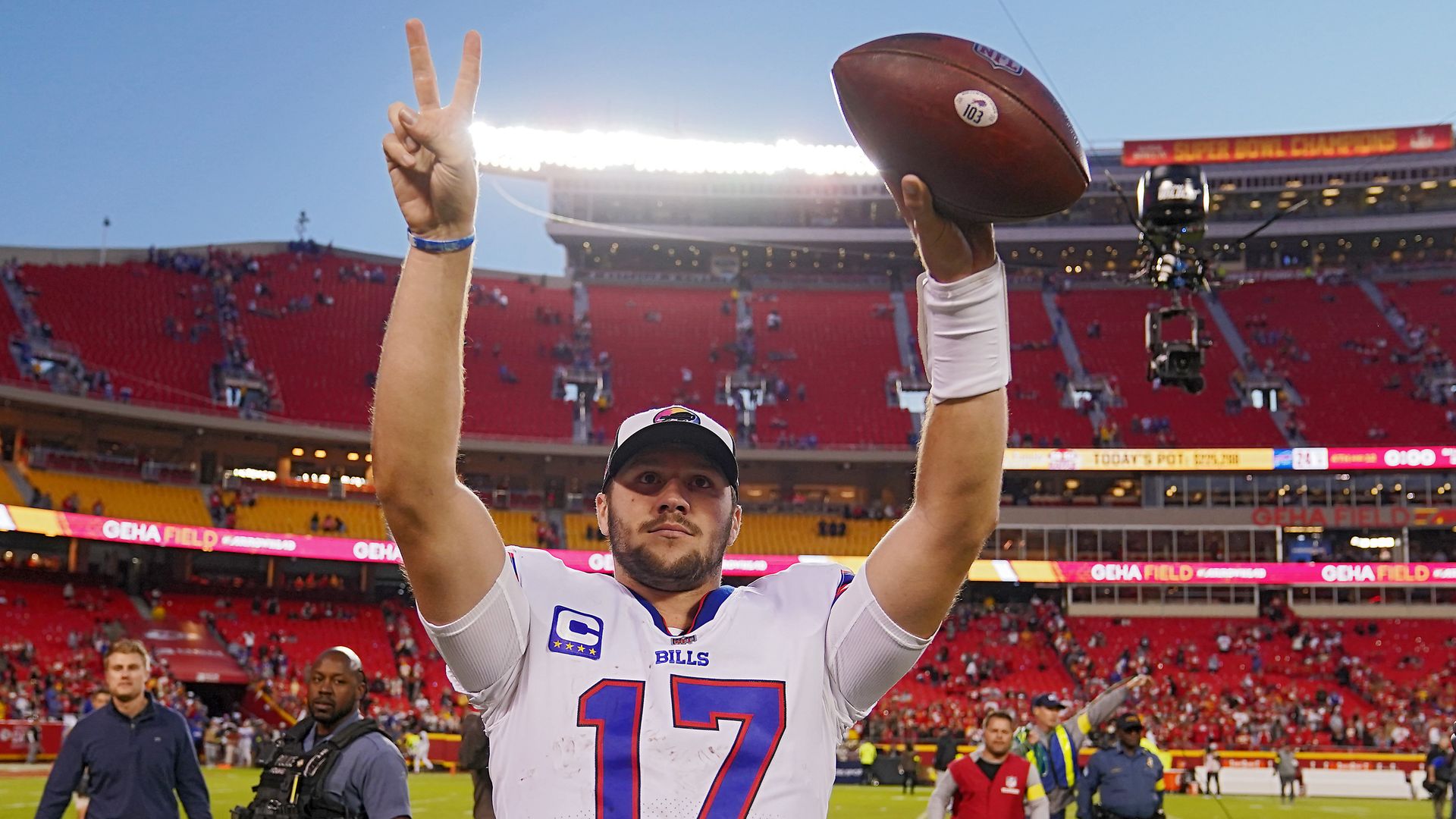 Buffalo Bills quarterback Josh Allen holds up a football and peace sign to fans in a stadium.