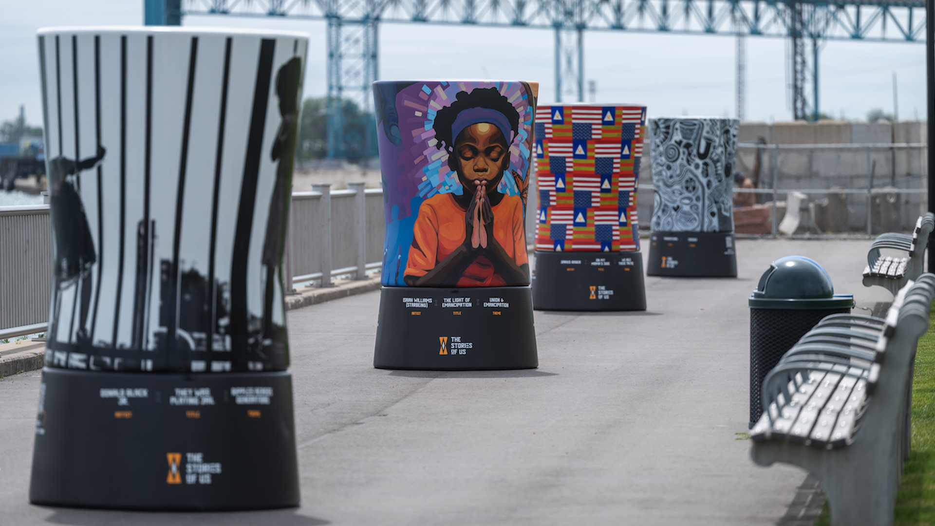 Drum-shaped art pieces along the riverfront, with the Detroit River behind them