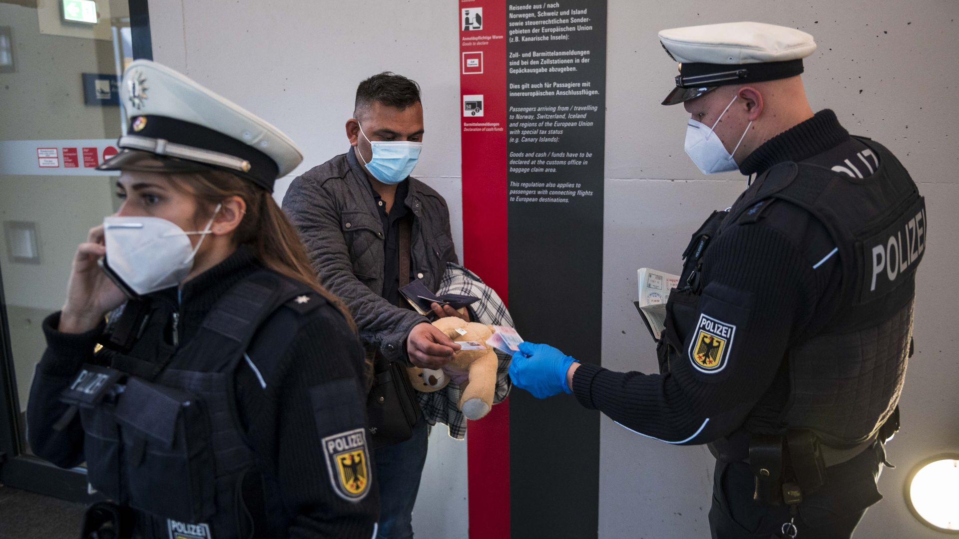 Photo of a masked police officer checking a masked passenger's documents 