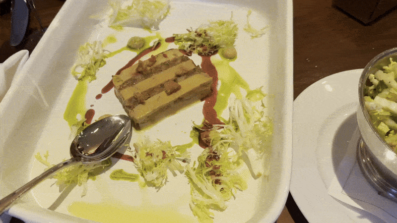 A camera pans over a table set with multiple dishes, including a salad, a gratin, a foie gras and a dish of leeks.