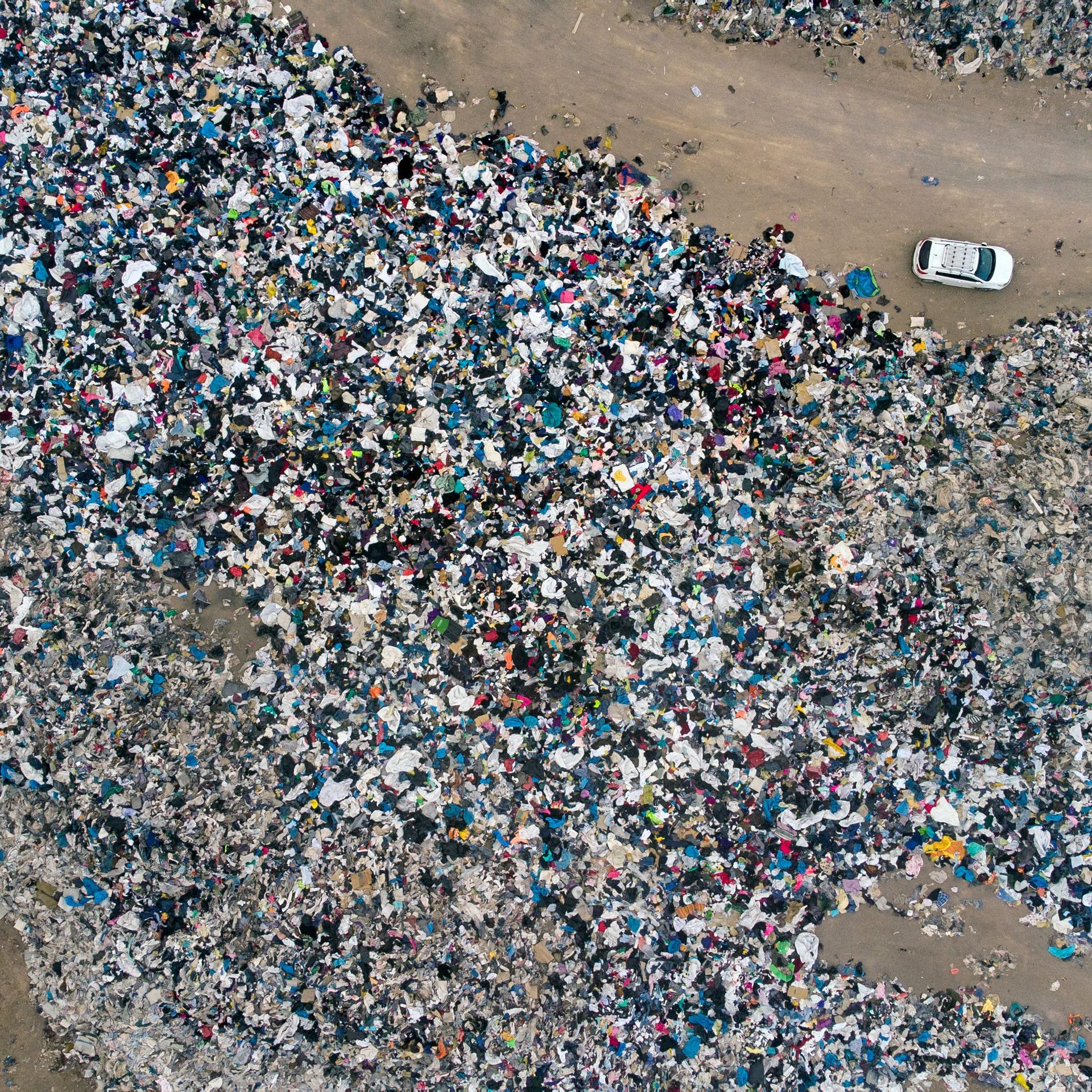 Tons of discarded clothing are piled up on a Chilean desert as a car drives through a dirt road
