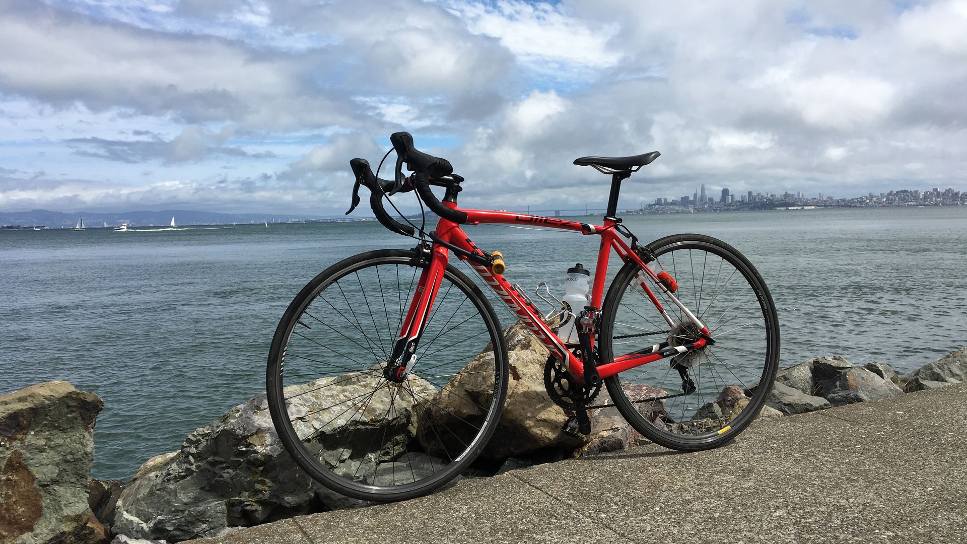 Photo of a red bike parked near the ocean. 