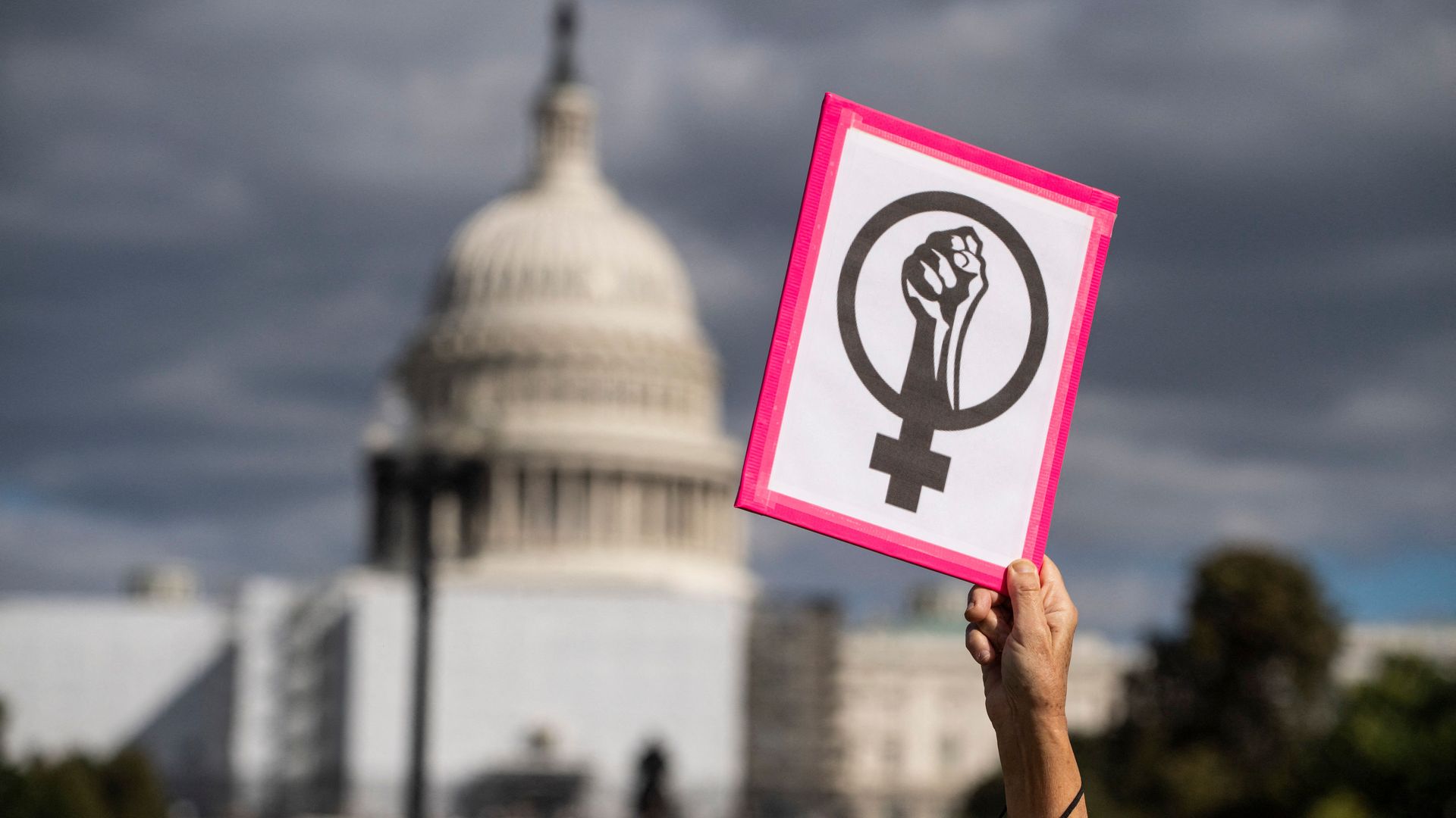 Photo of a hand raising an abortion rights sign against the backdrop of the U.S. Capitol