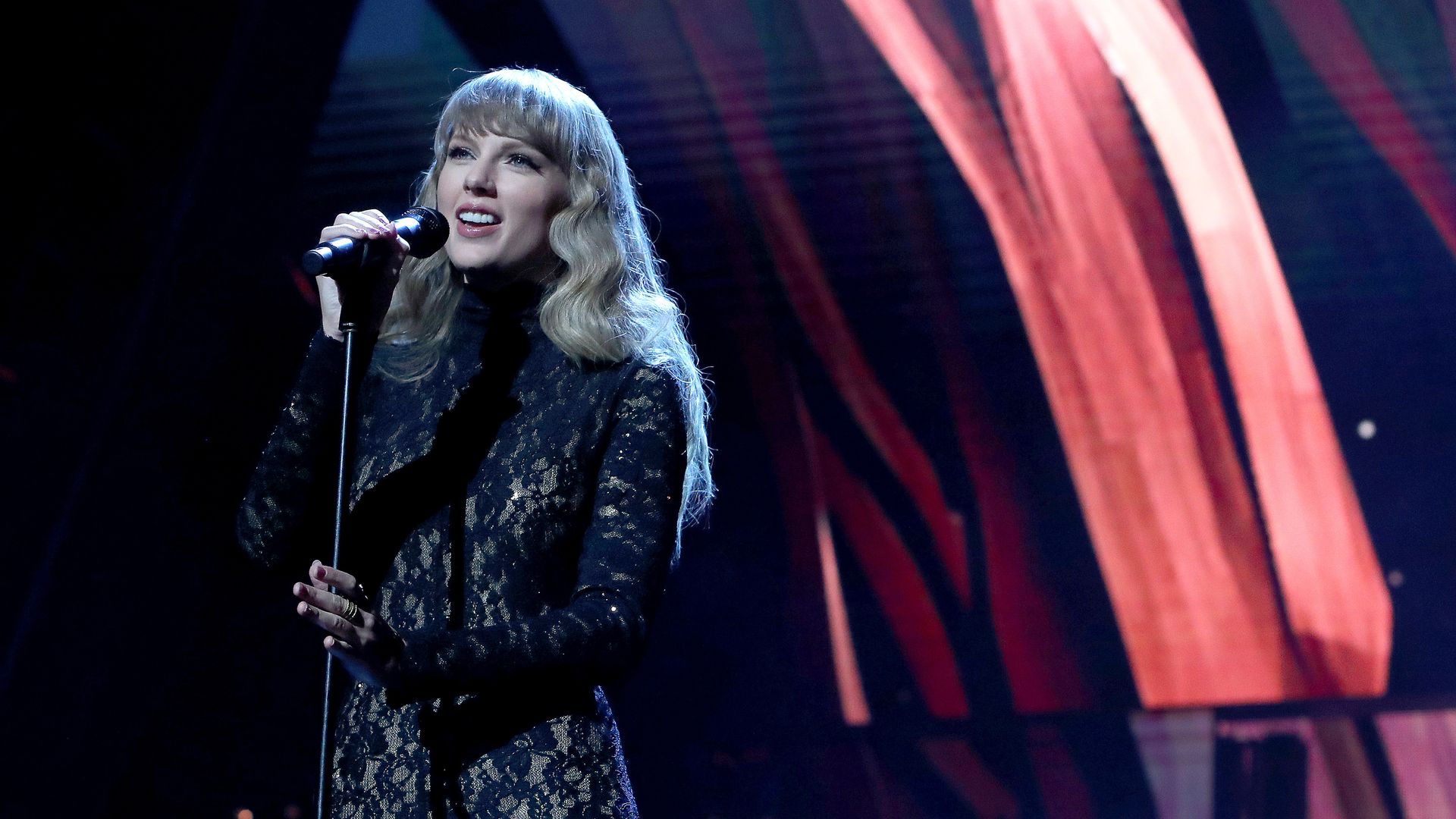 Taylor Swift sings at a microphone stand in a black body suit