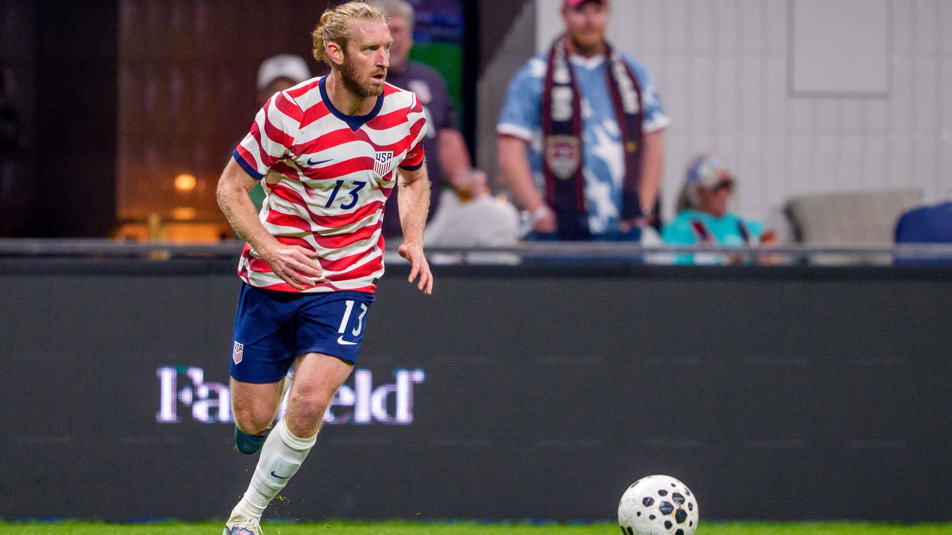 Tim Ream in red, white and blue USMNT kit dribbles a soccer ball during a game. 