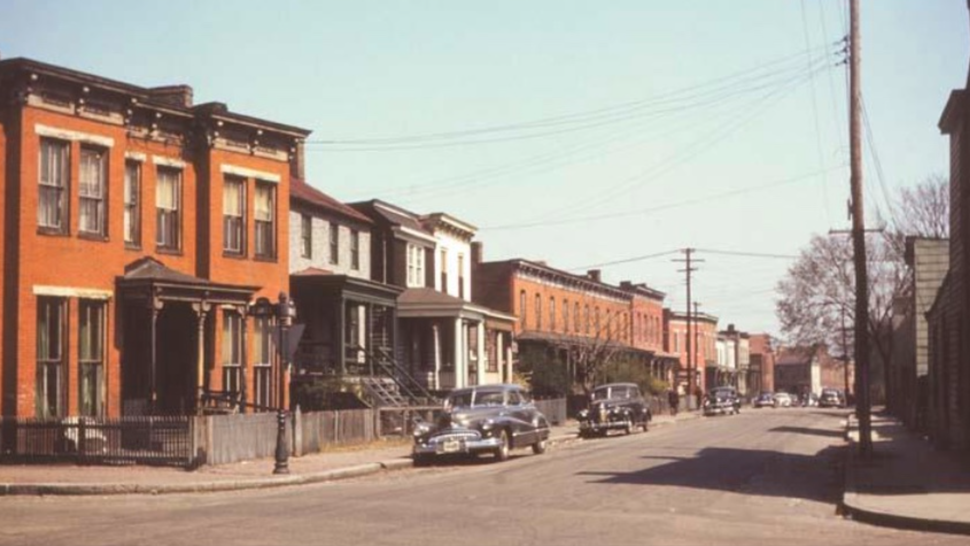An archival photo of a line of houses with cars.