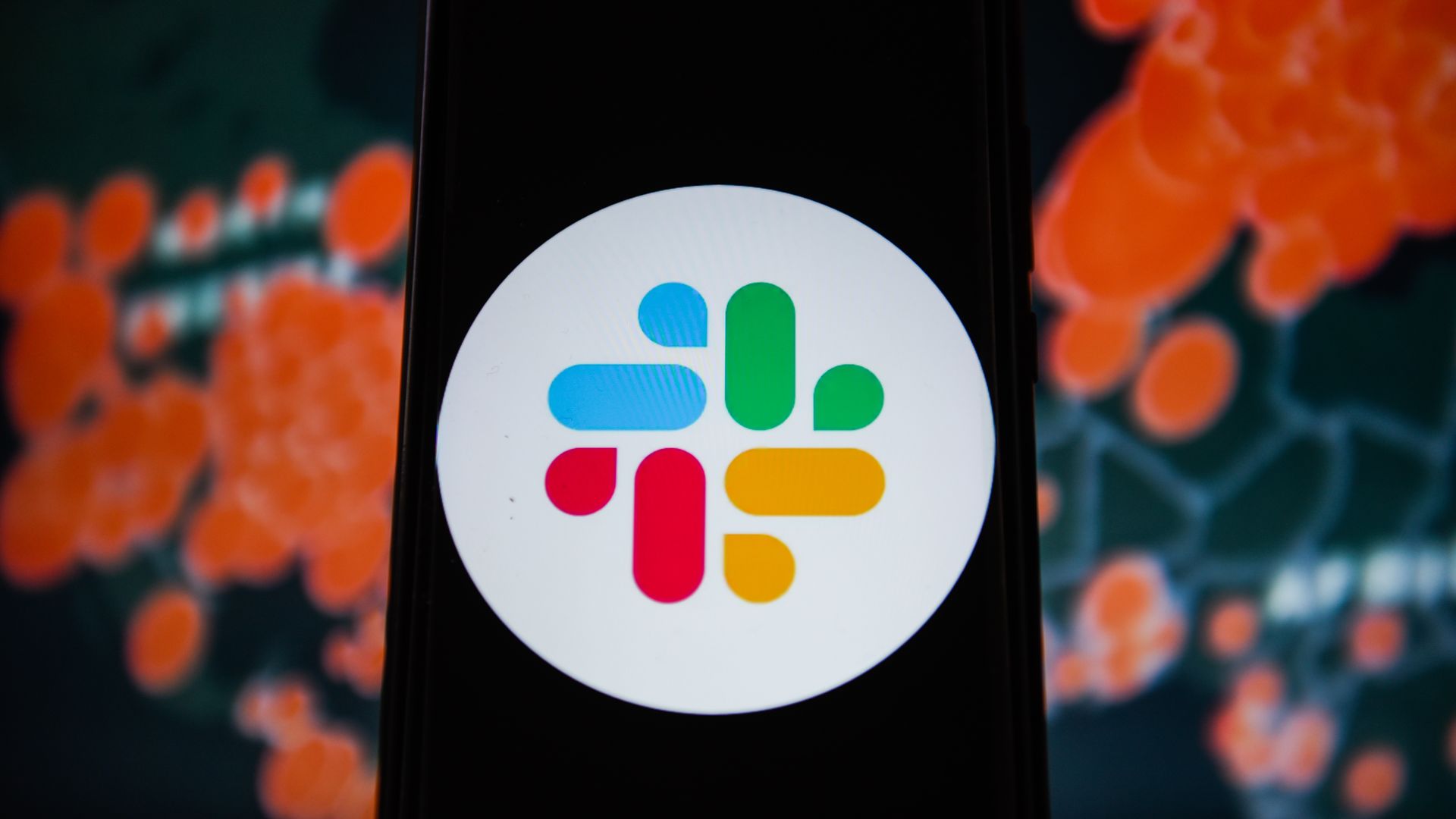 The Slack app logo on a phone screen with a map in the background detailing the coronavirus outbreak