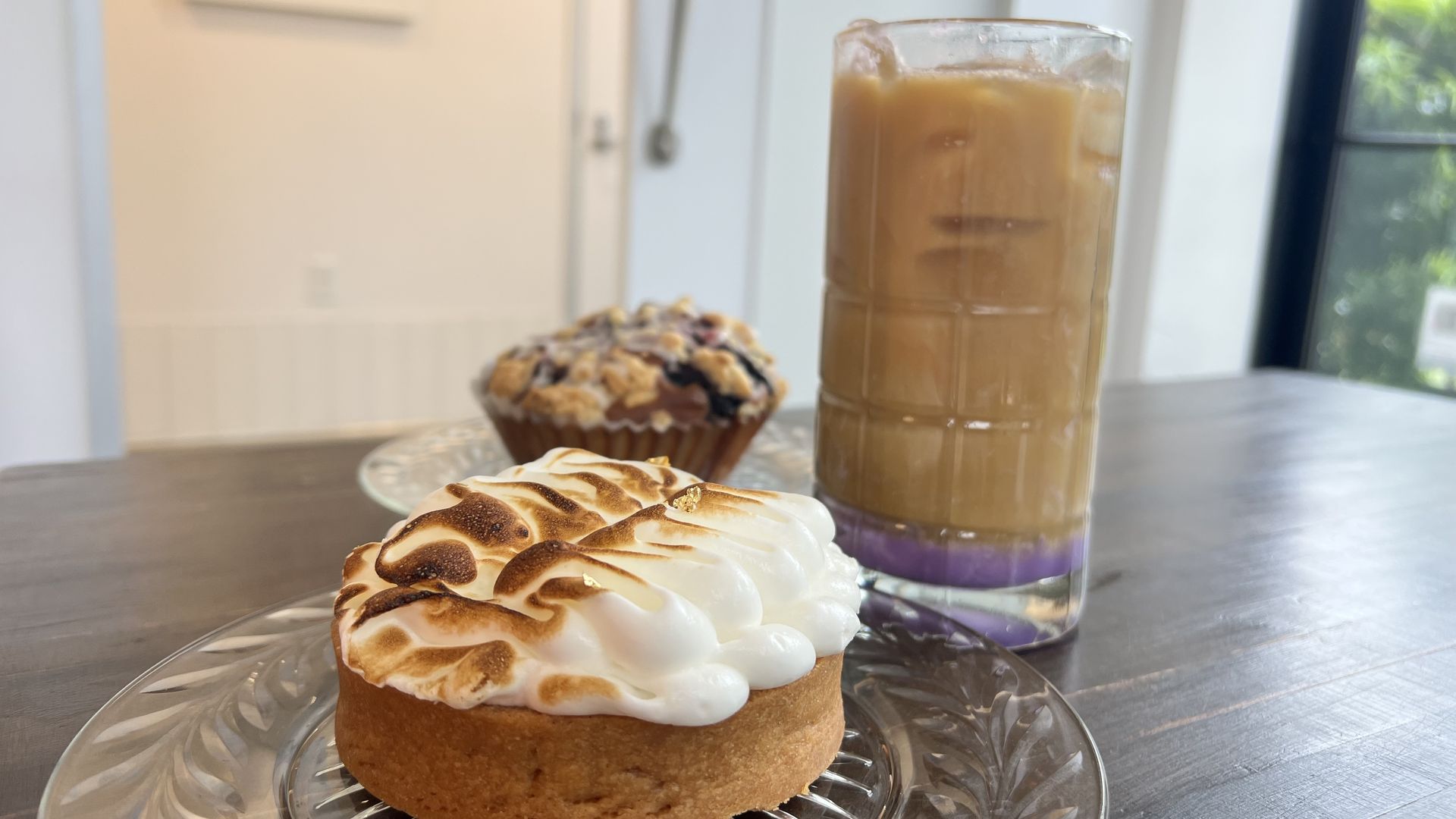 Photo of a drink with purple ube on the bottom, a tarte and a blueberry muffin. 