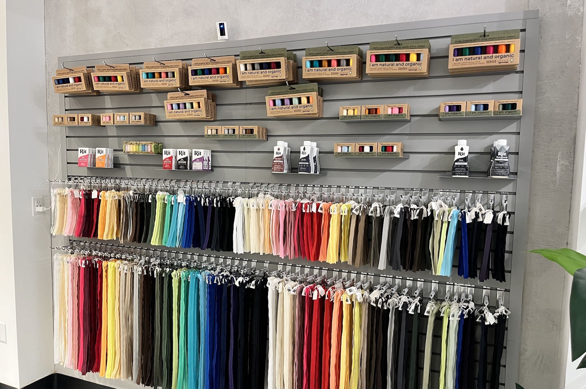 Store display of rainbow fabric ribbons hanging on a wall, with upper shelves of boxes labeled i am natural and organic and Rit dye products on the lower shelves.