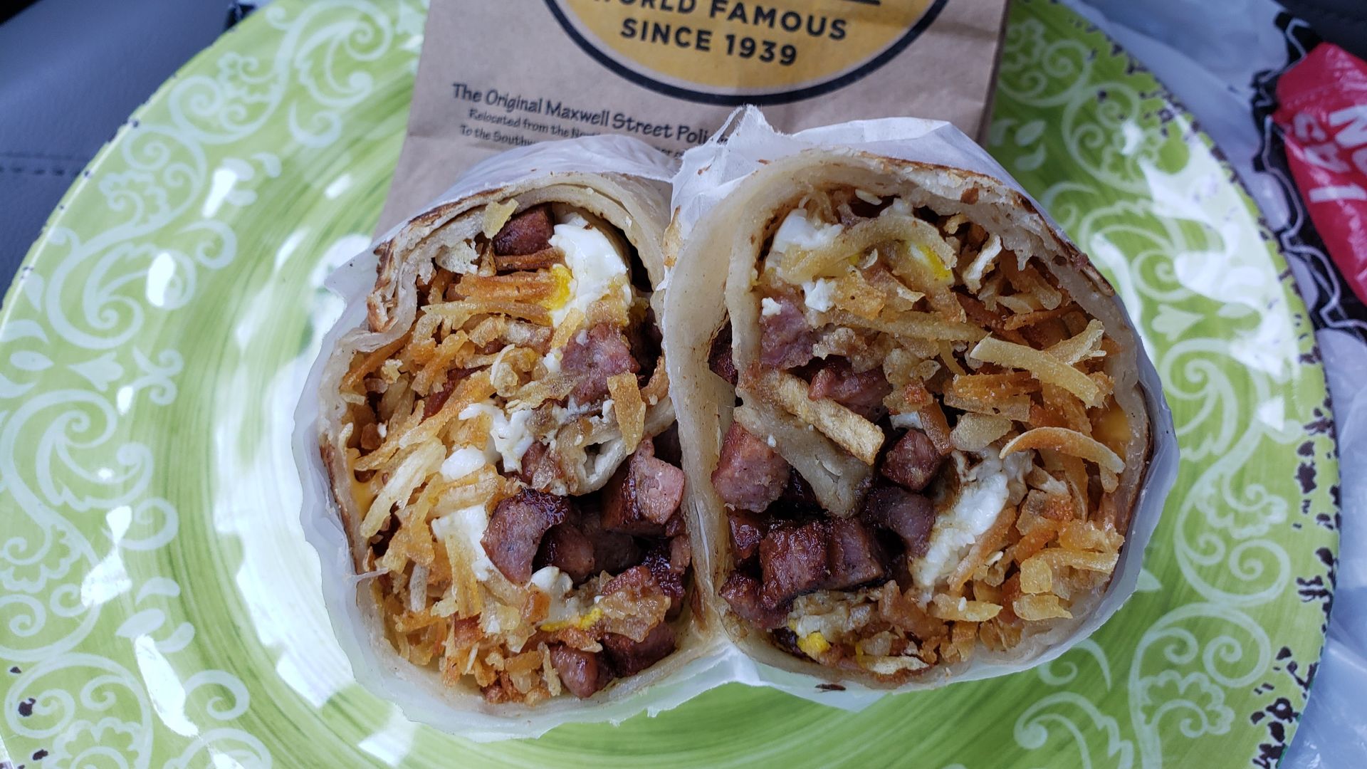 Inside of a burrito with hash browns, sausage, eggs and on a green plate.