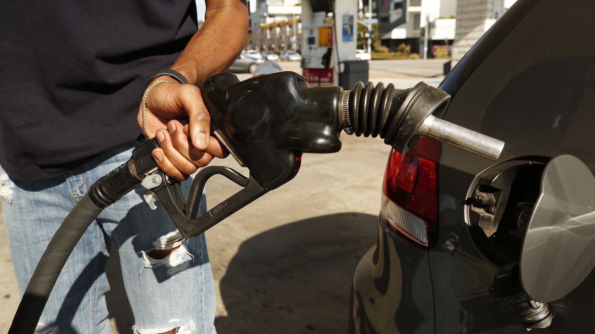 A person holds a gas pump near his car