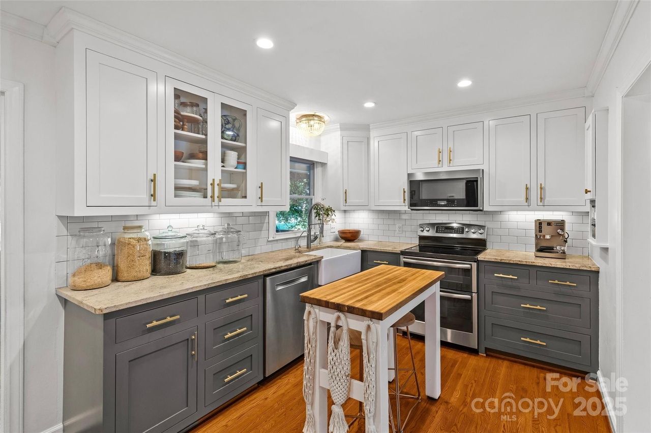 Modern kitchen with white upper cabinets, gray lower cabinets, marble countertops, subway tile backsplash, stainless steel appliances, wooden island, and hardwood flooring.