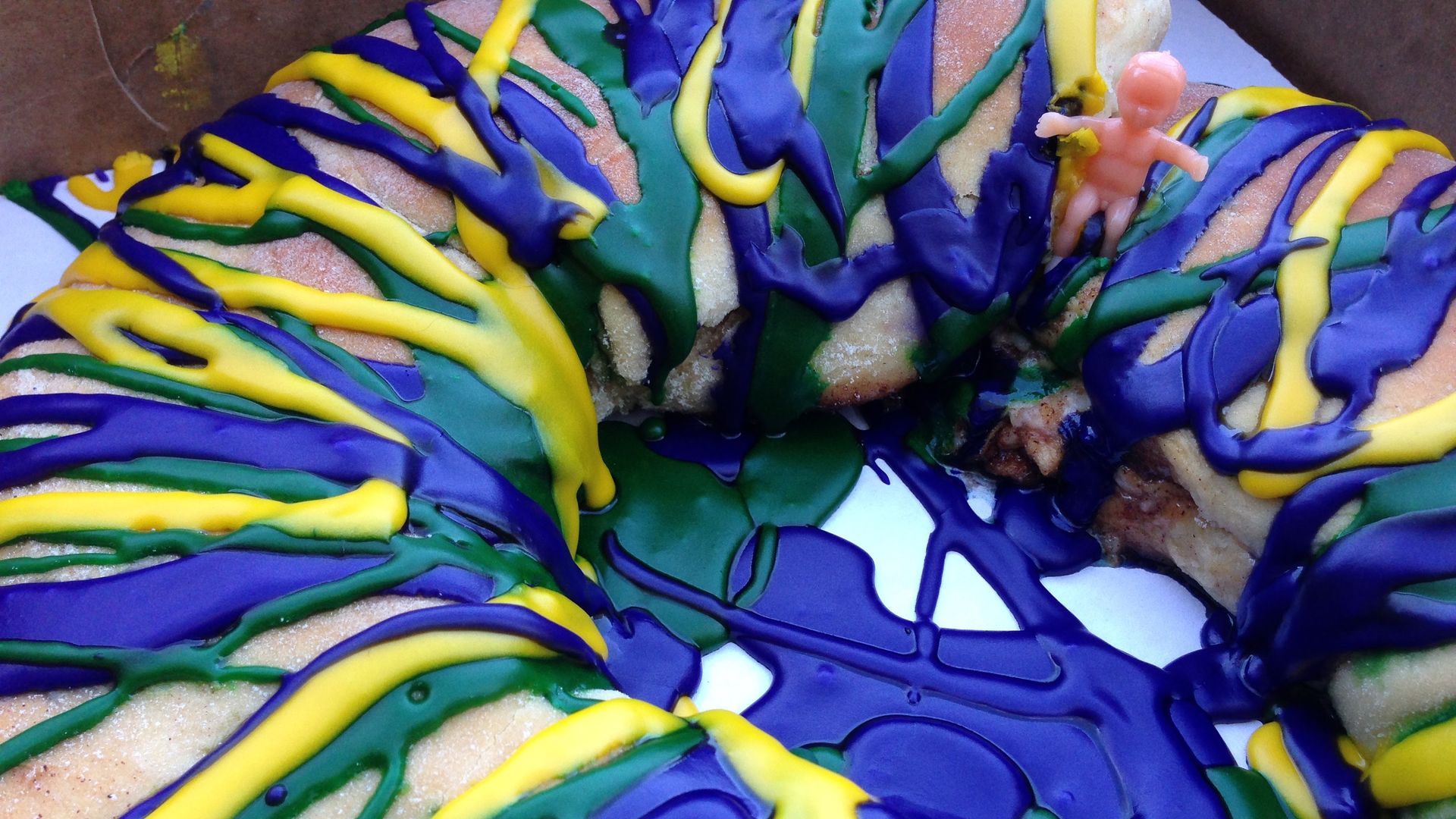 Photo shows a circular king cake covered in brightly colored purple, green and gold frosting.