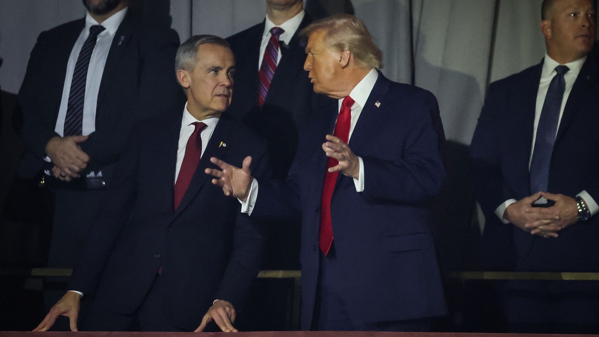 President Trump and Canadian PM Mark Carney, in suits and red ties, speaking to each other while standing, with Trump gesturing. 