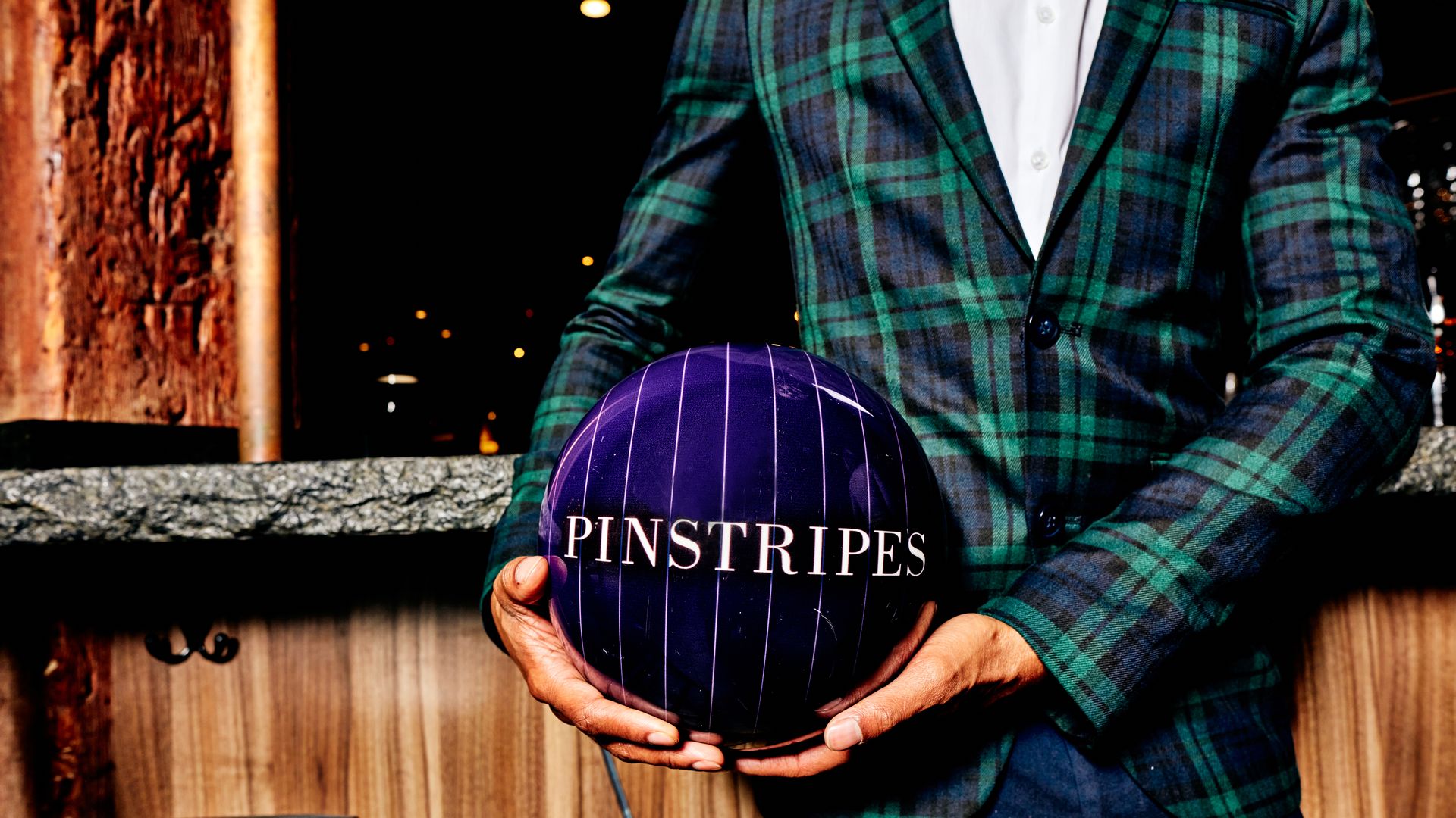 A person in a striped suit holds a purple bowling ball that says "Pinstripes" on it.