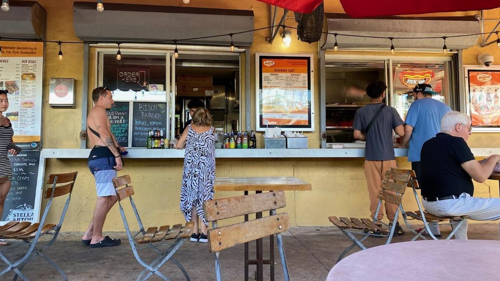 People stand at a walk-up food counter on a sunny day 