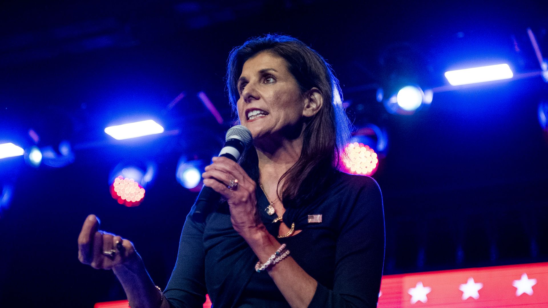 NIkki Haley, wearing a blue blouse, speaks to a crowd with a microphone.