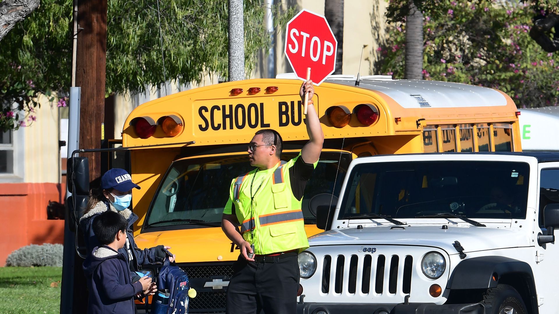 A man in a neon yellow vest holds up a stop sign in front of a school bus.