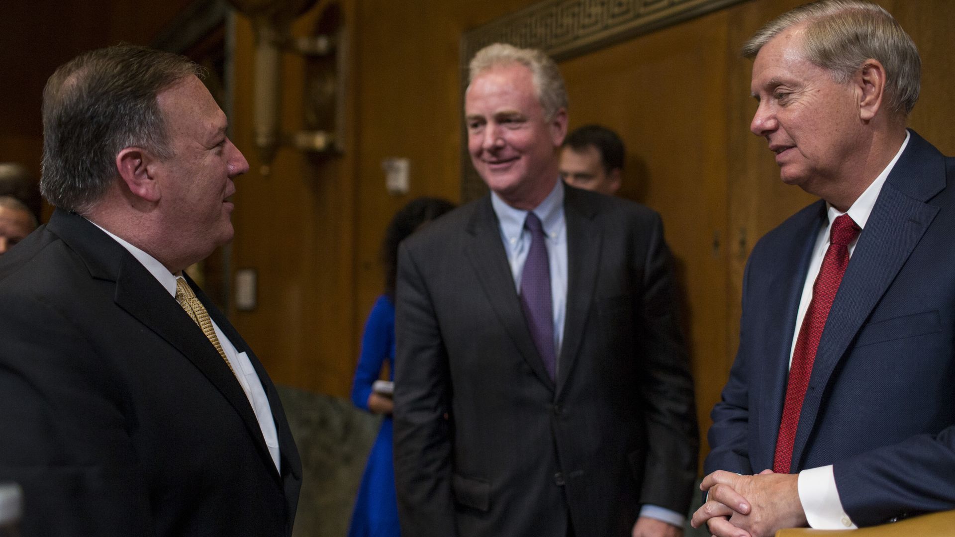 In this image, Graham and Van Hollen speak with Mike Pompeo. All are wearing suits and standing in front of a wooden panel wall