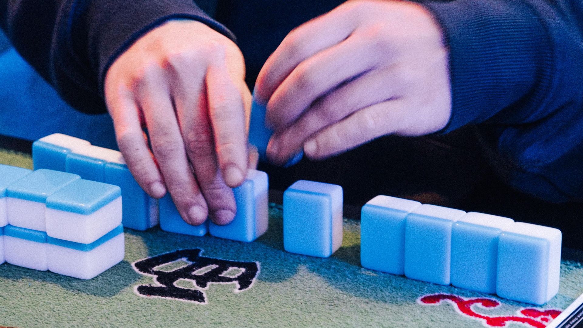 Photo of two hands shuffling tiles on a mahjong board