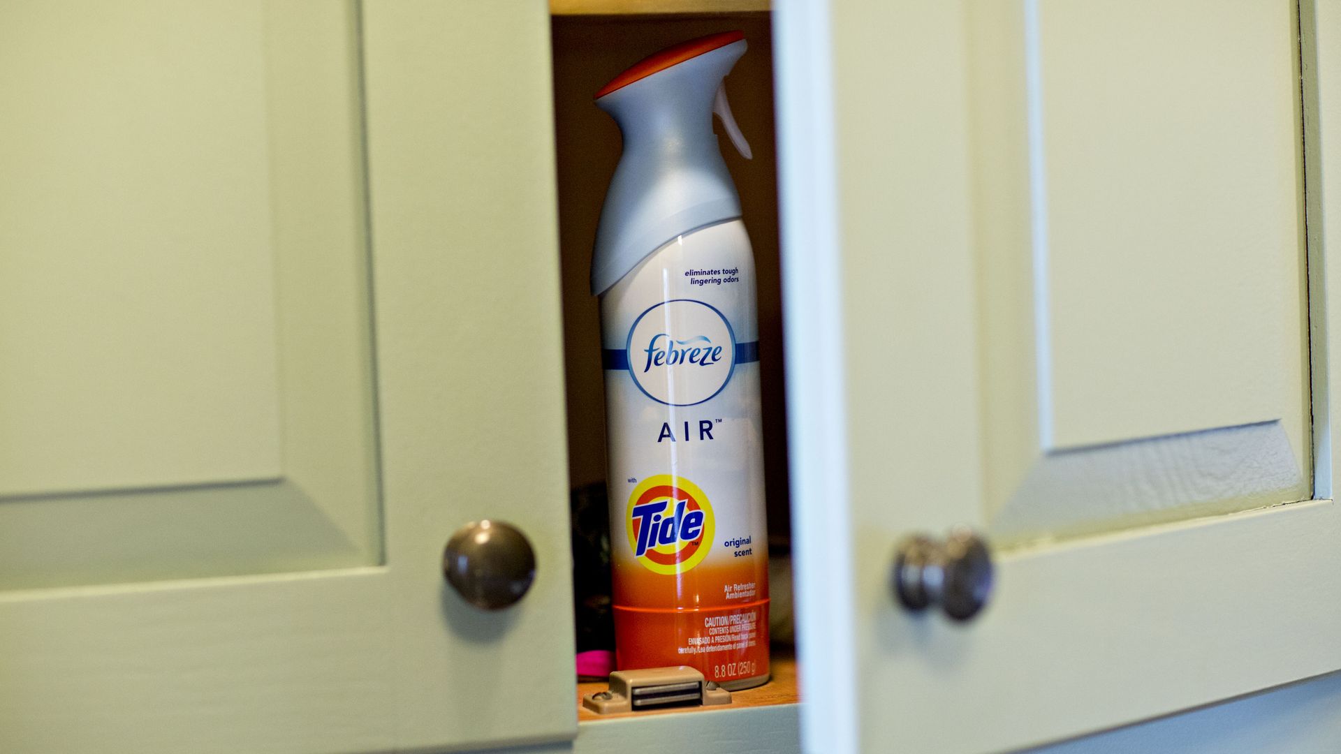 A canister of Febreze in a kitchen cabinet.
