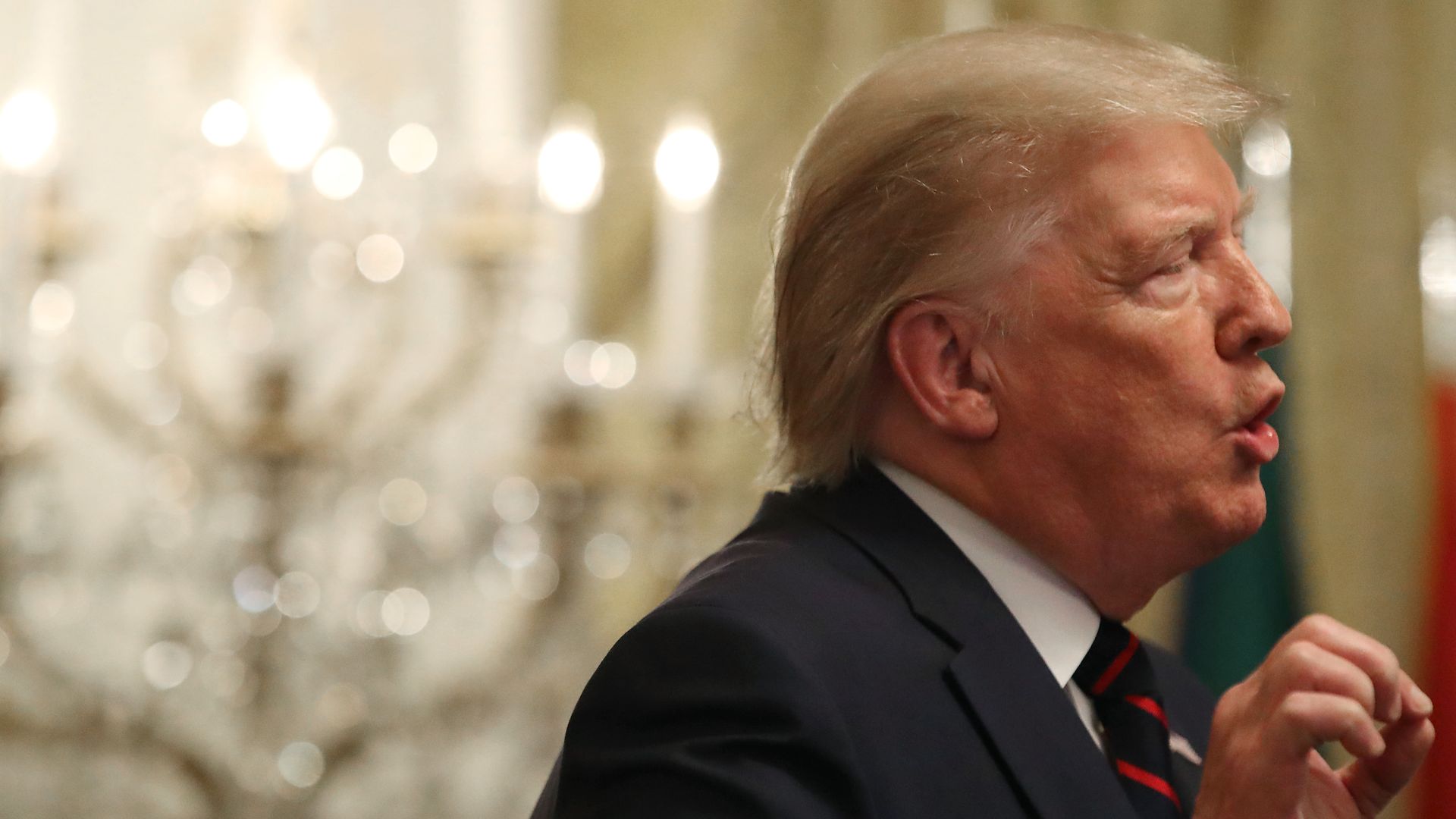 In this image, Trump speaks and there is a chandelier in the background behind him.