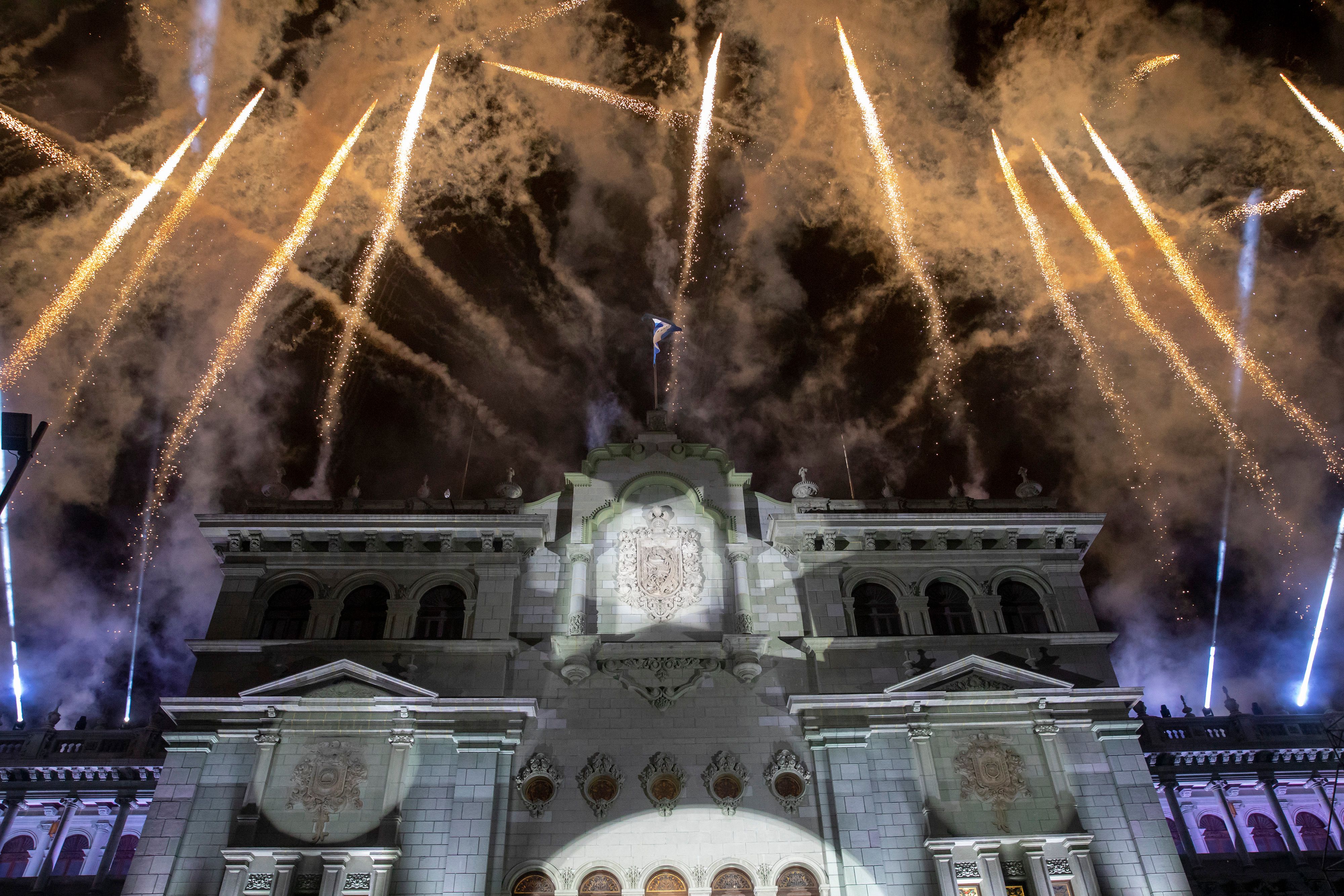 Fireworks are seen in the nighttime sky behind Guatemala's National Palace, which is a white old building with several stories