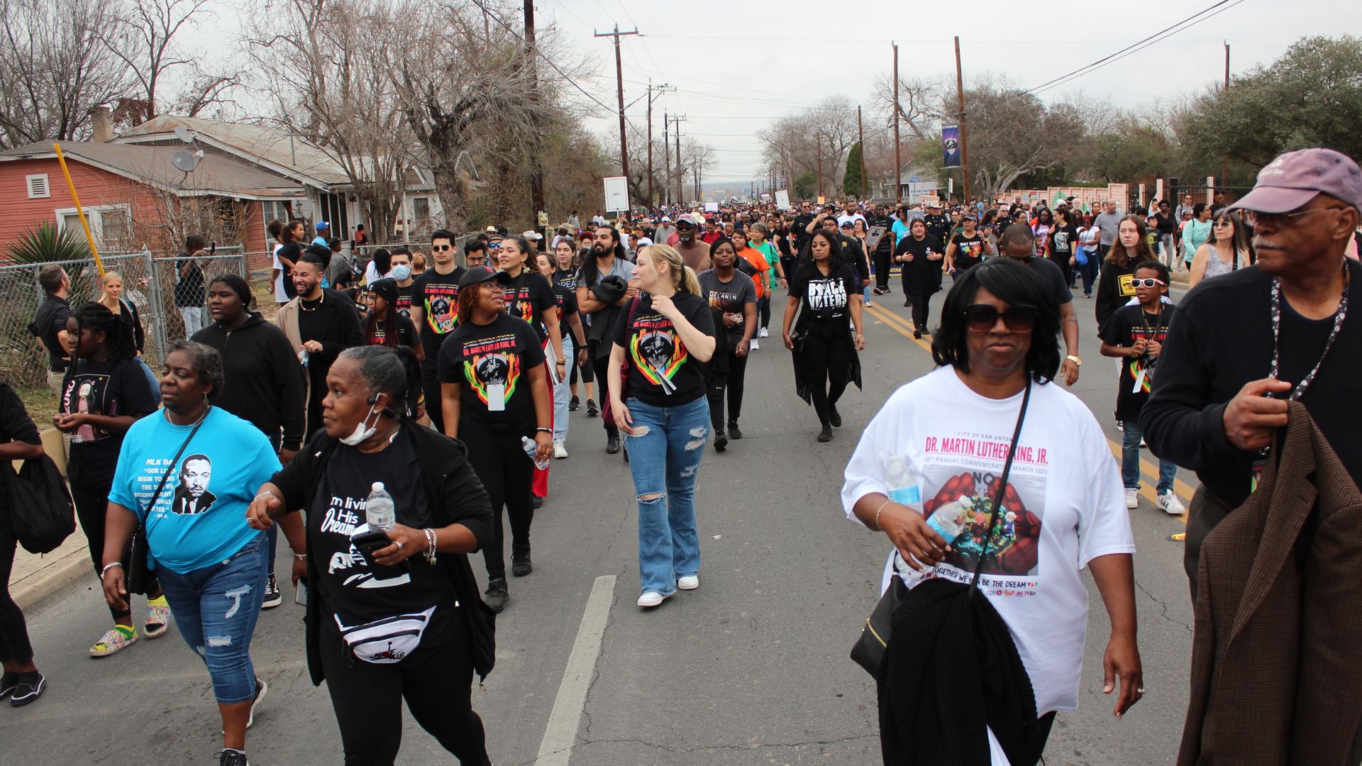 A large crowd of people walk in groups down a neighborhood road.