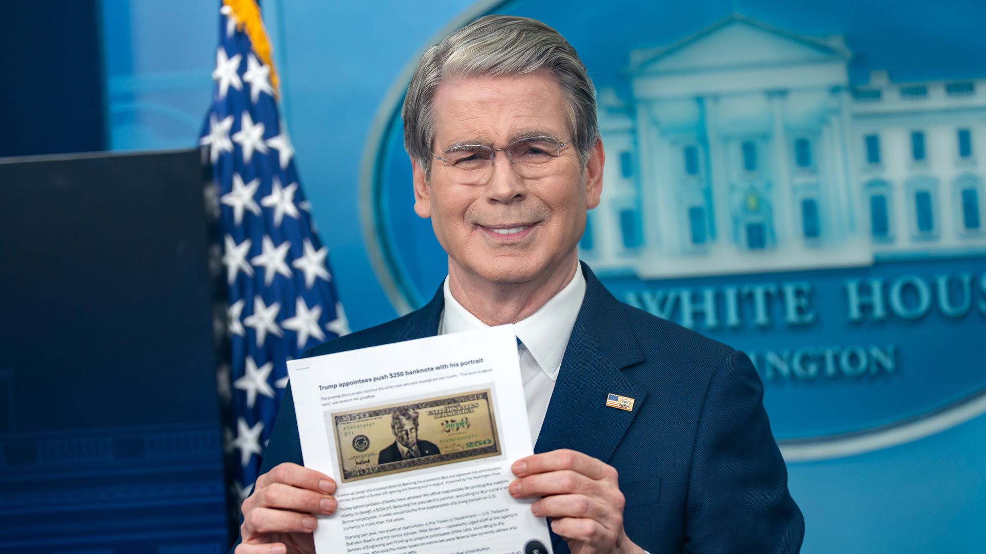 Treasury Secretary Scott Bessent — wearing a dark blue suit, a white collared shirt and an American flag pin during a press briefing — holds a print-out of an article that includes a photo of a $250 bill design with President Trump's face on it.