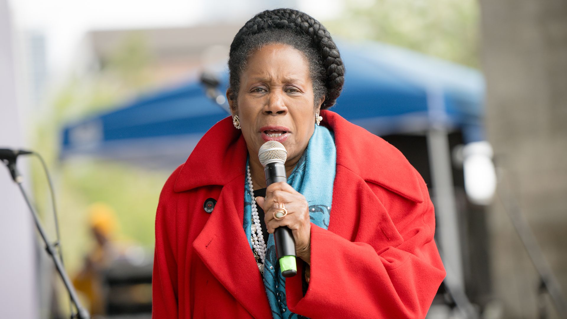 Rep. Sheila Jackson Lee, wearing a blue top and red jacket, speaks into a microphone 