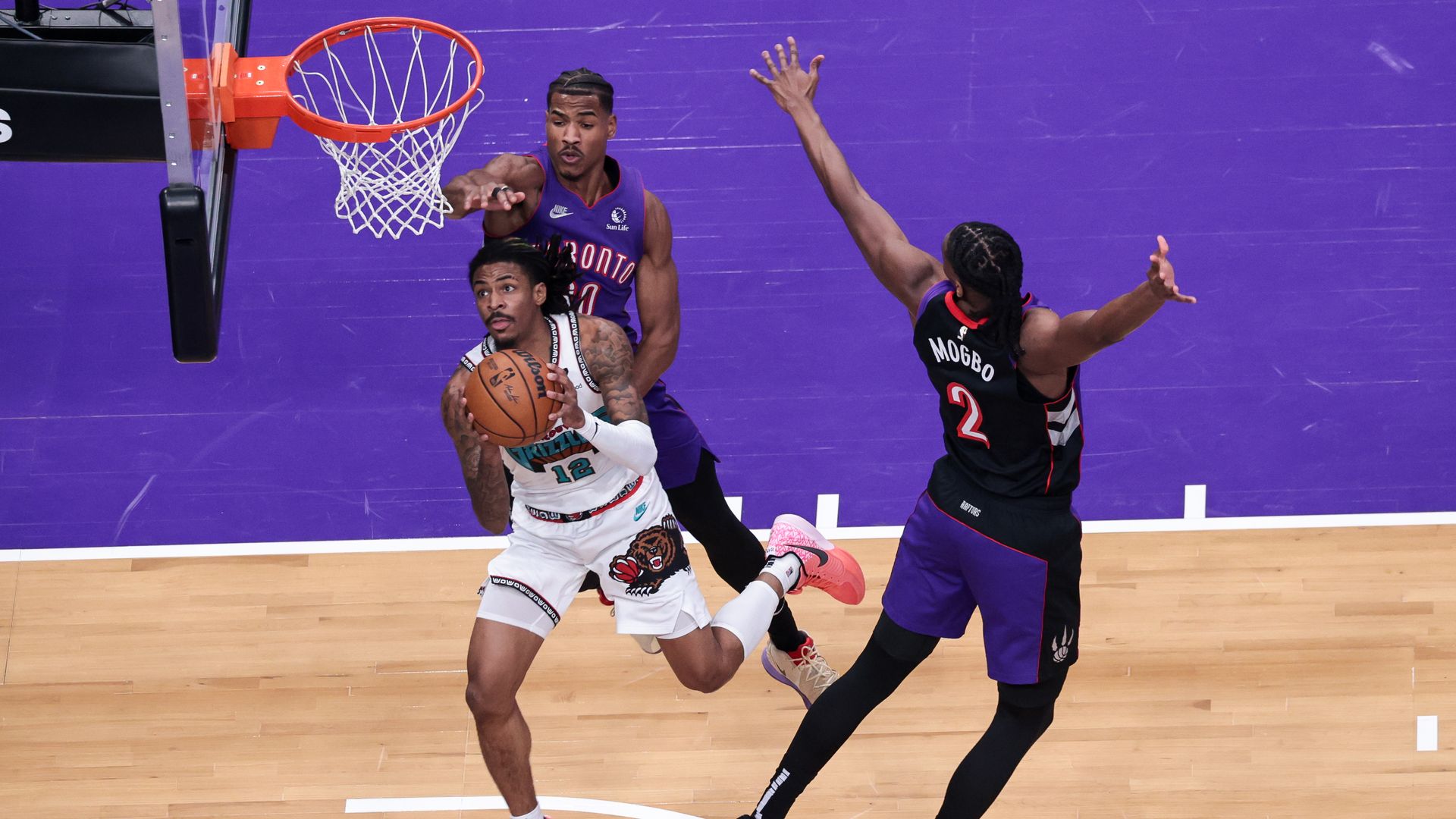 A NBA player driving the basket past two defenders.