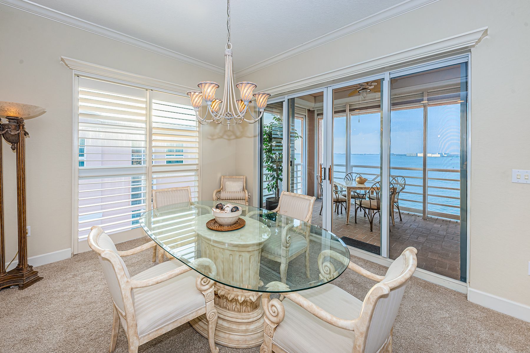 A room with a glass-top dining table set with a sliding door out to a patio overlooking the water.