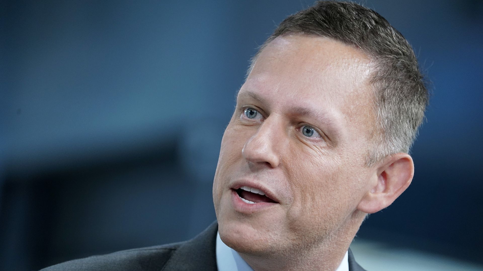 In this image, Peter Thiel wears a tie and suit and talks
