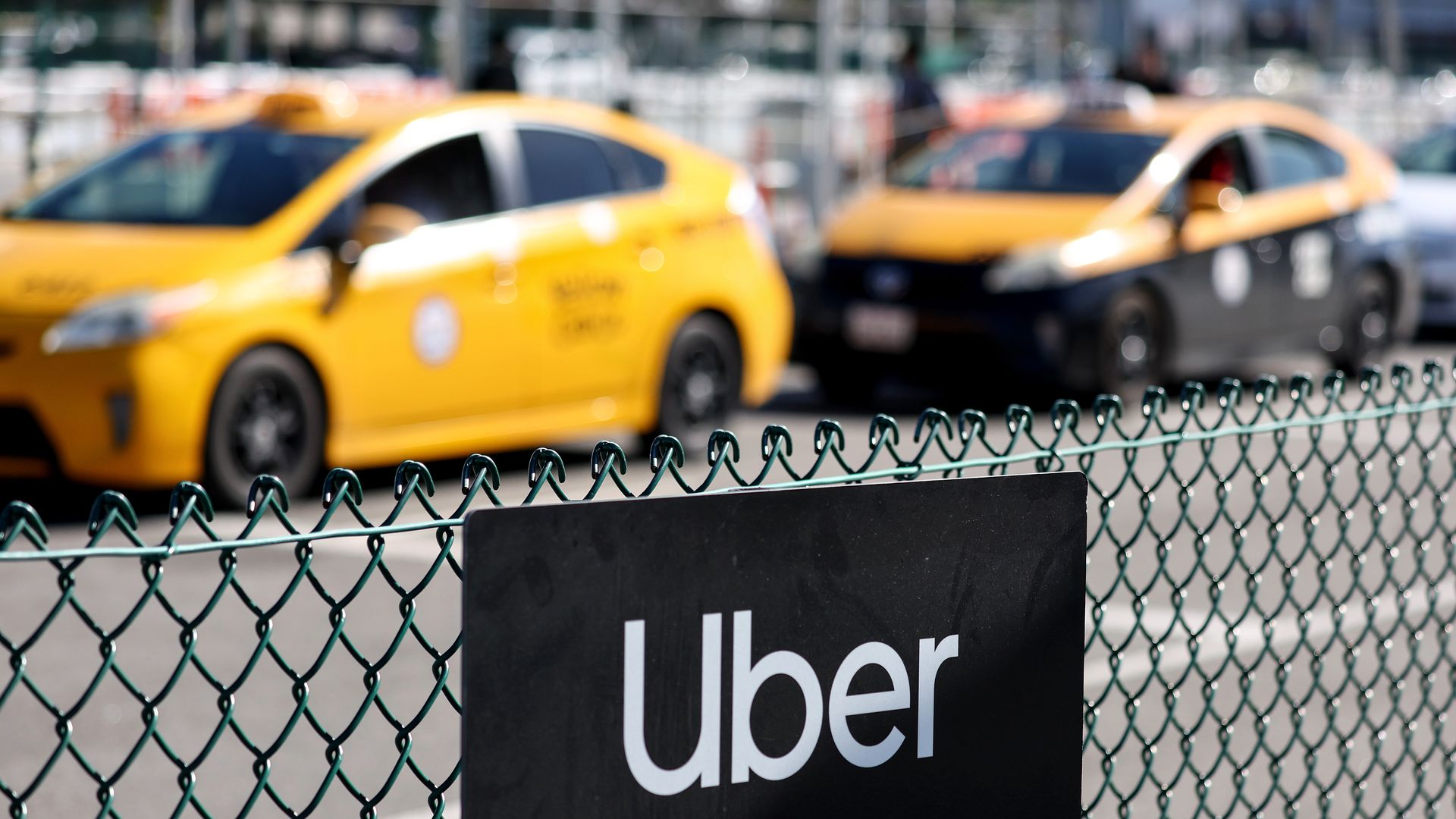  An Uber rideshare sign is posted on a fence as taxis wait in the background. 