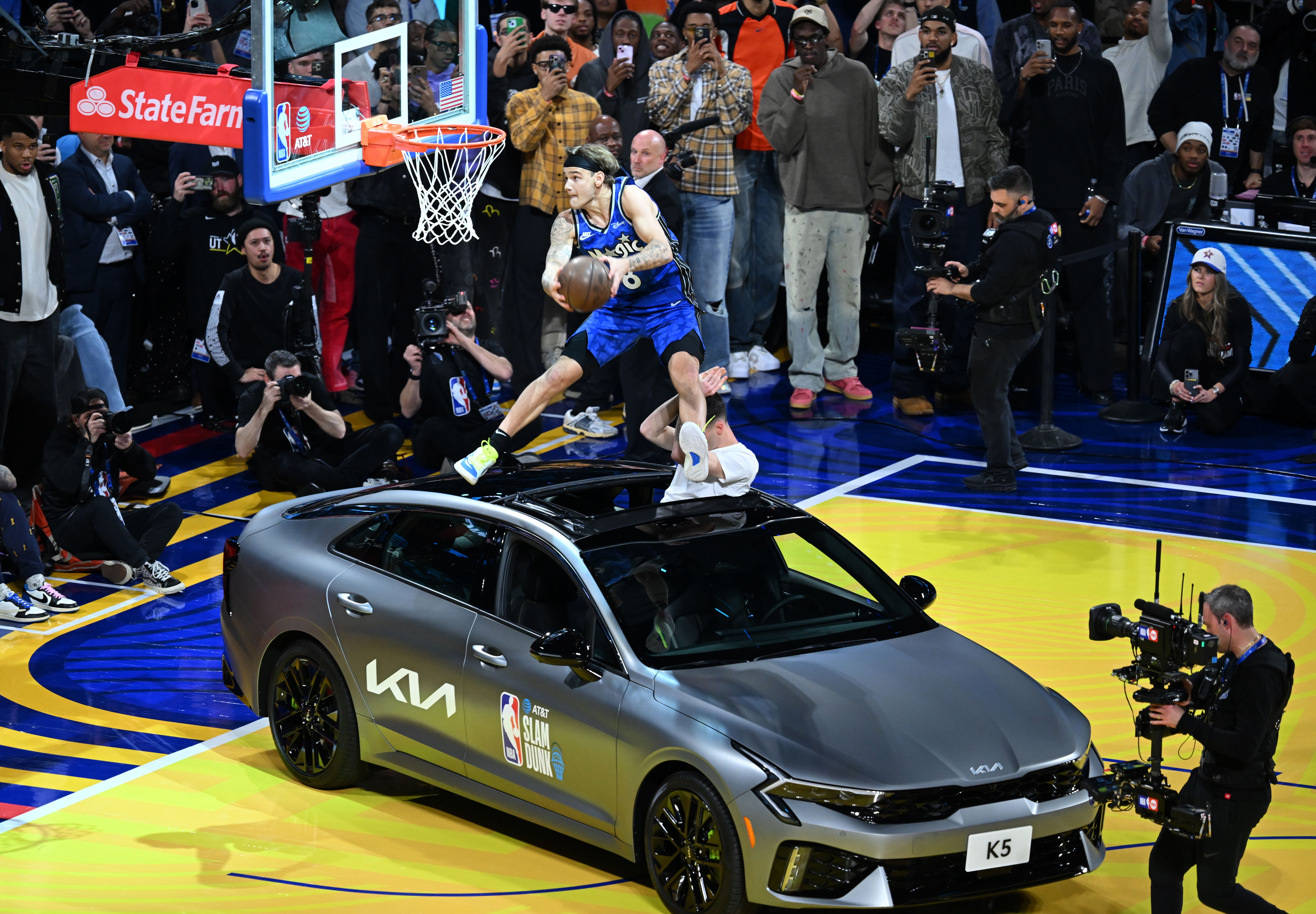 A basketball player jumps over a car to dunk the ball