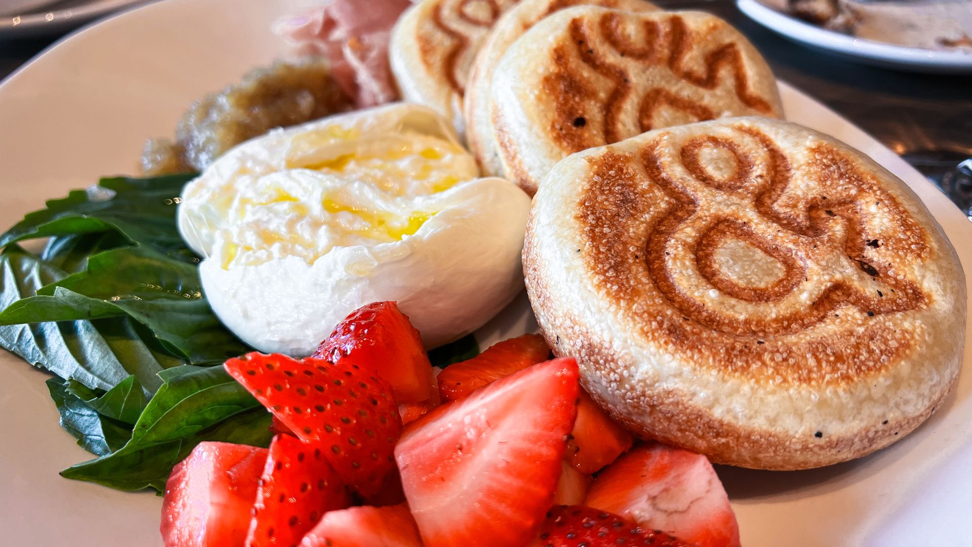 Four pieces of circular bread, burrata, strawberries, and basil on a white plate. 