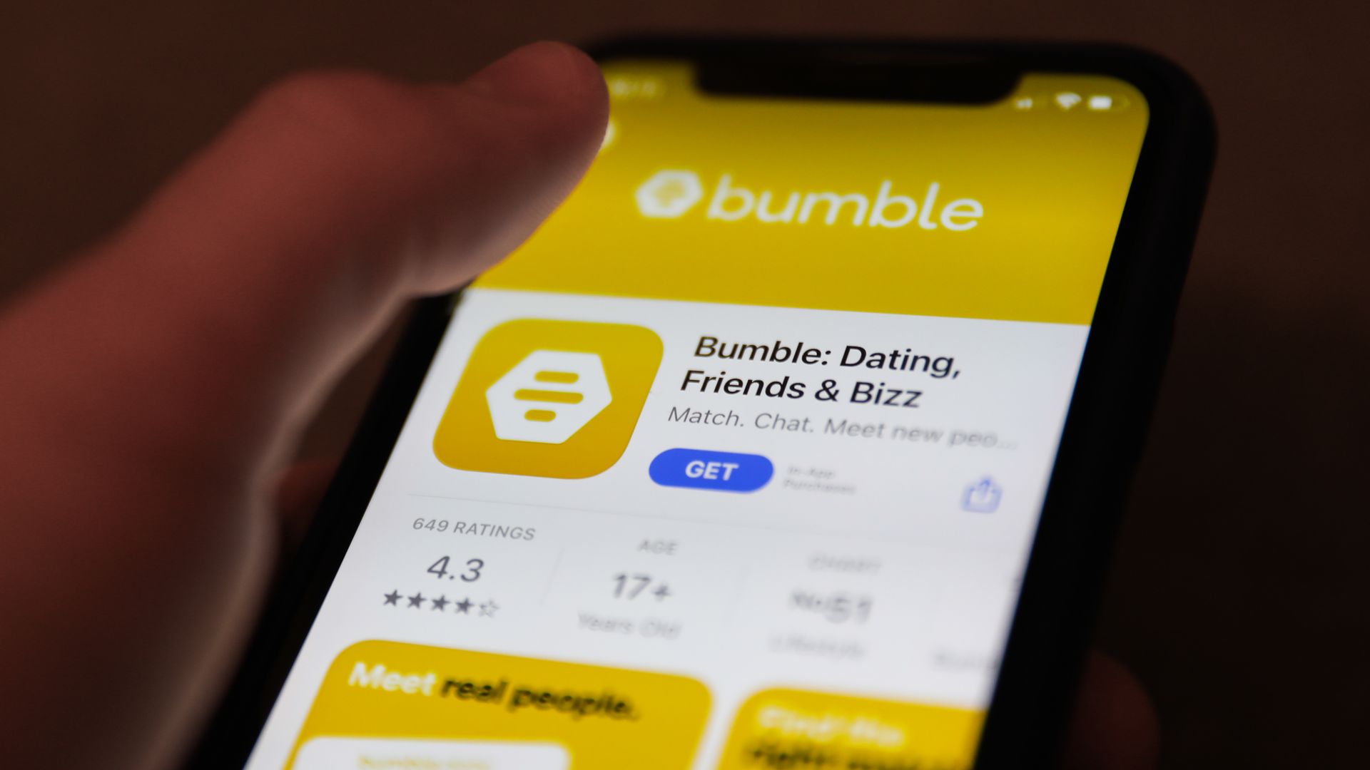 A photo of a hand holding a phone with the Bumble app on display.